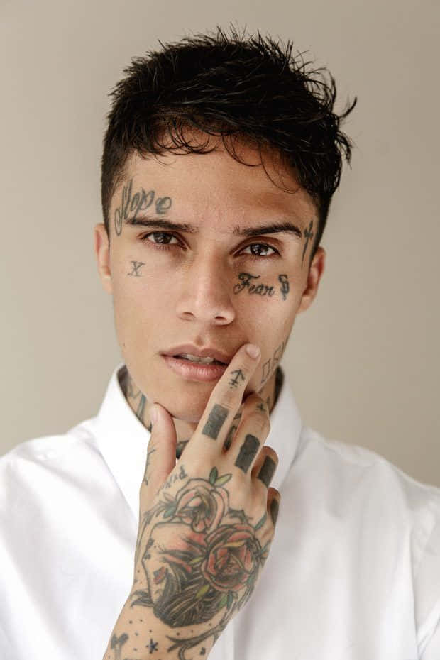 Face Tattoo 桌布 壁紙 — 一名年輕男子，臉上紋有「希望」和「恐懼」字樣，手上紋有玫瑰圖案，身穿白色襯衫。