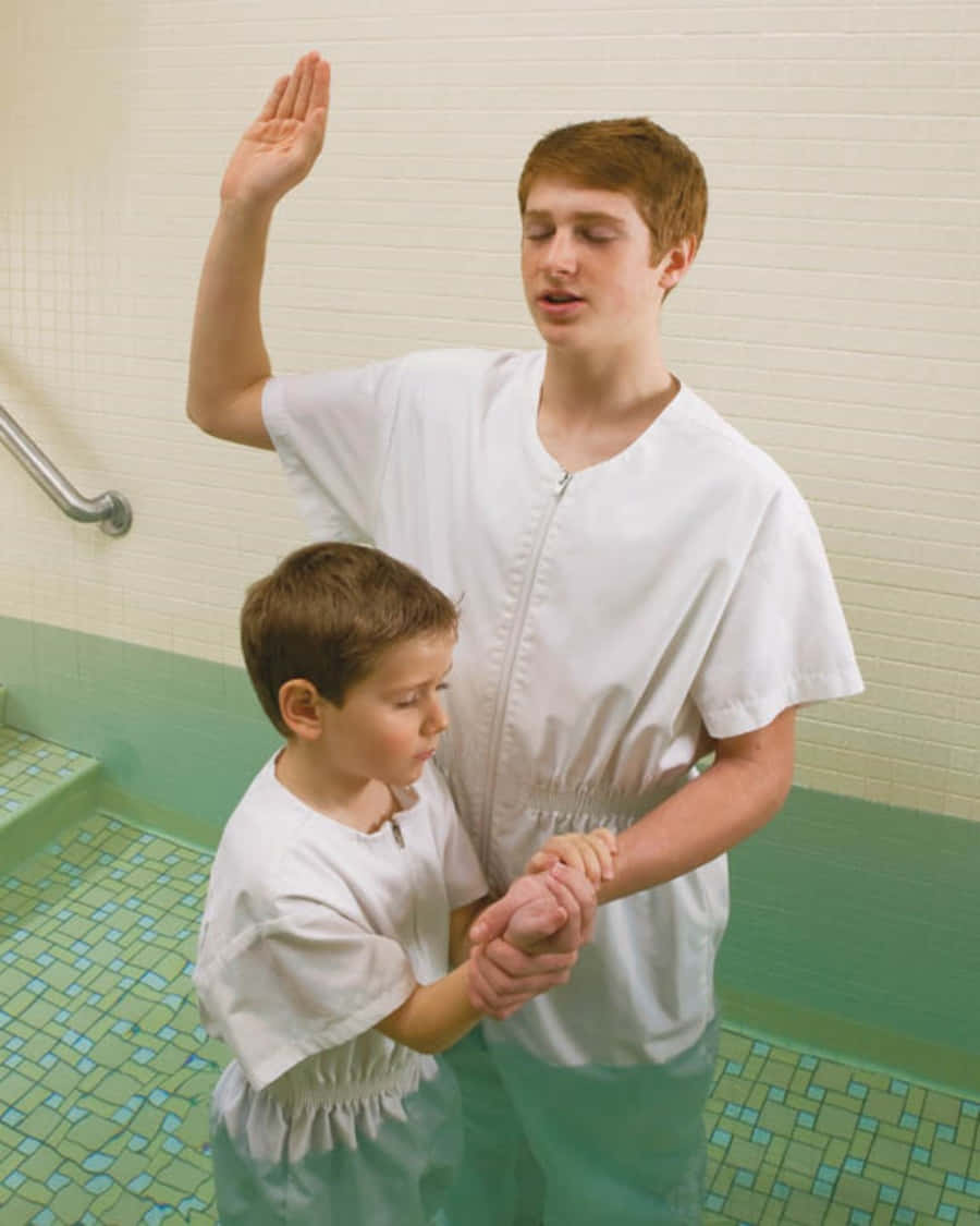 Baptism 桌布 壁紙 — 一名年輕男子和男孩身穿白色長袍，站在瓷磚洗禮池中，一人舉手，另一人莊嚴地握著手。