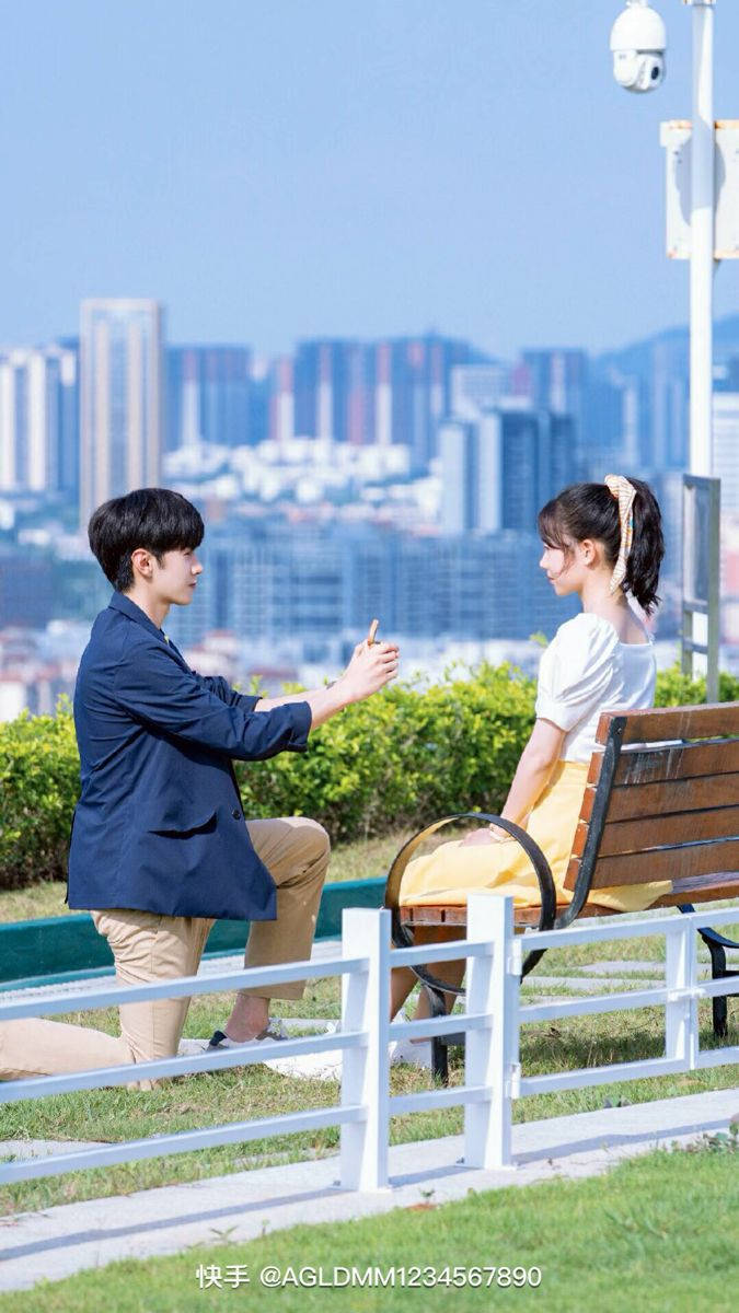 Couples 桌布 壁紙 — 一名年輕男子單膝跪地，向坐在陽光普照的城市公園中的女子求婚，背景是城市天際線。