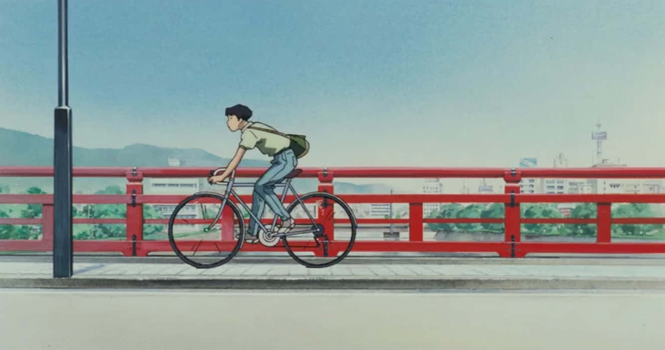 Studio Ghibli Ocean Waves 桌布 壁紙 — 一名年輕男子在晴朗的藍天下，騎著腳踏車穿過一座鮮紅色的橋，遠處有山脈和城市景觀。
