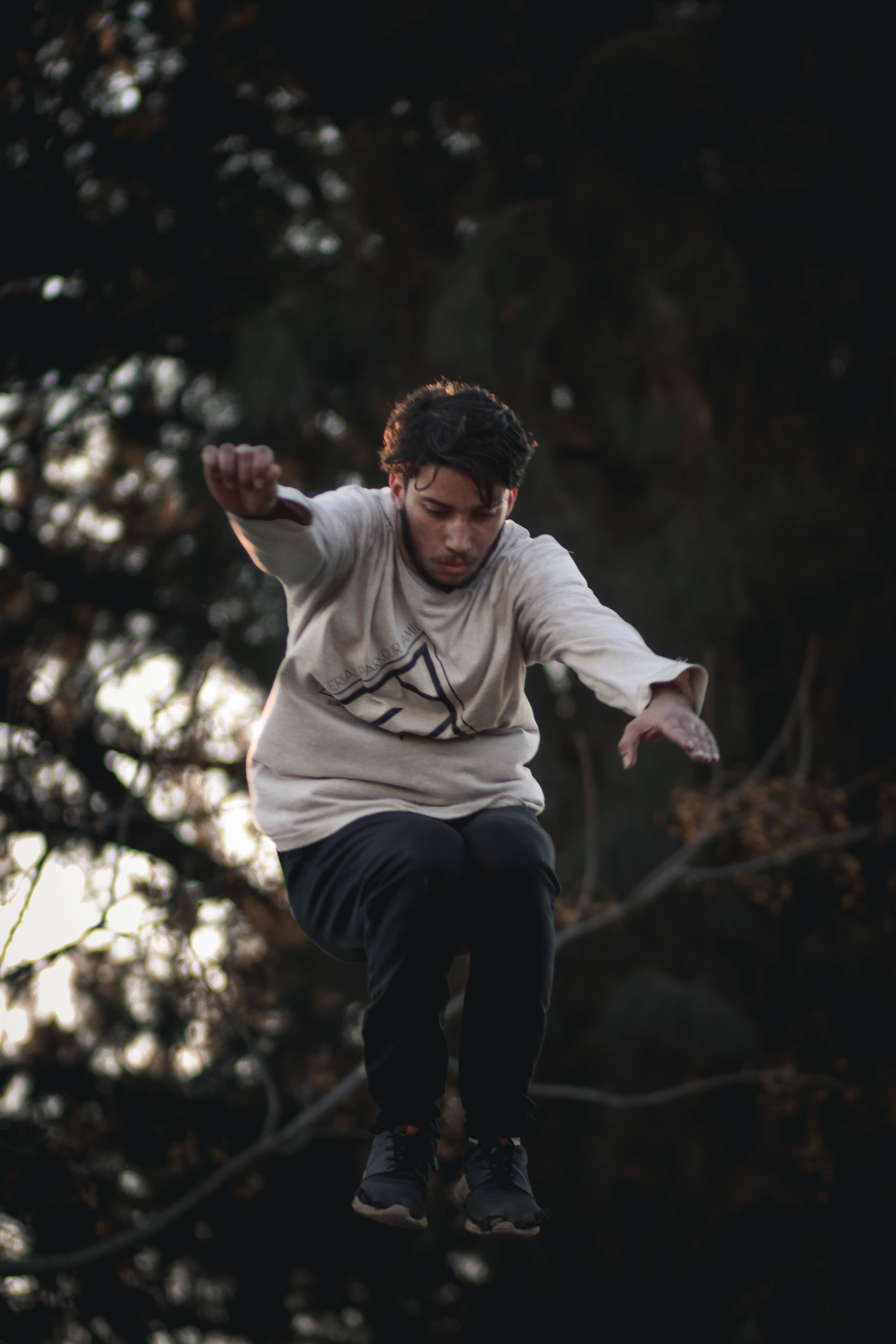 Parkour 桌布 壁紙 — 一名年輕男子在空中跳躍，背景是深色樹木，帶有柔和背光。