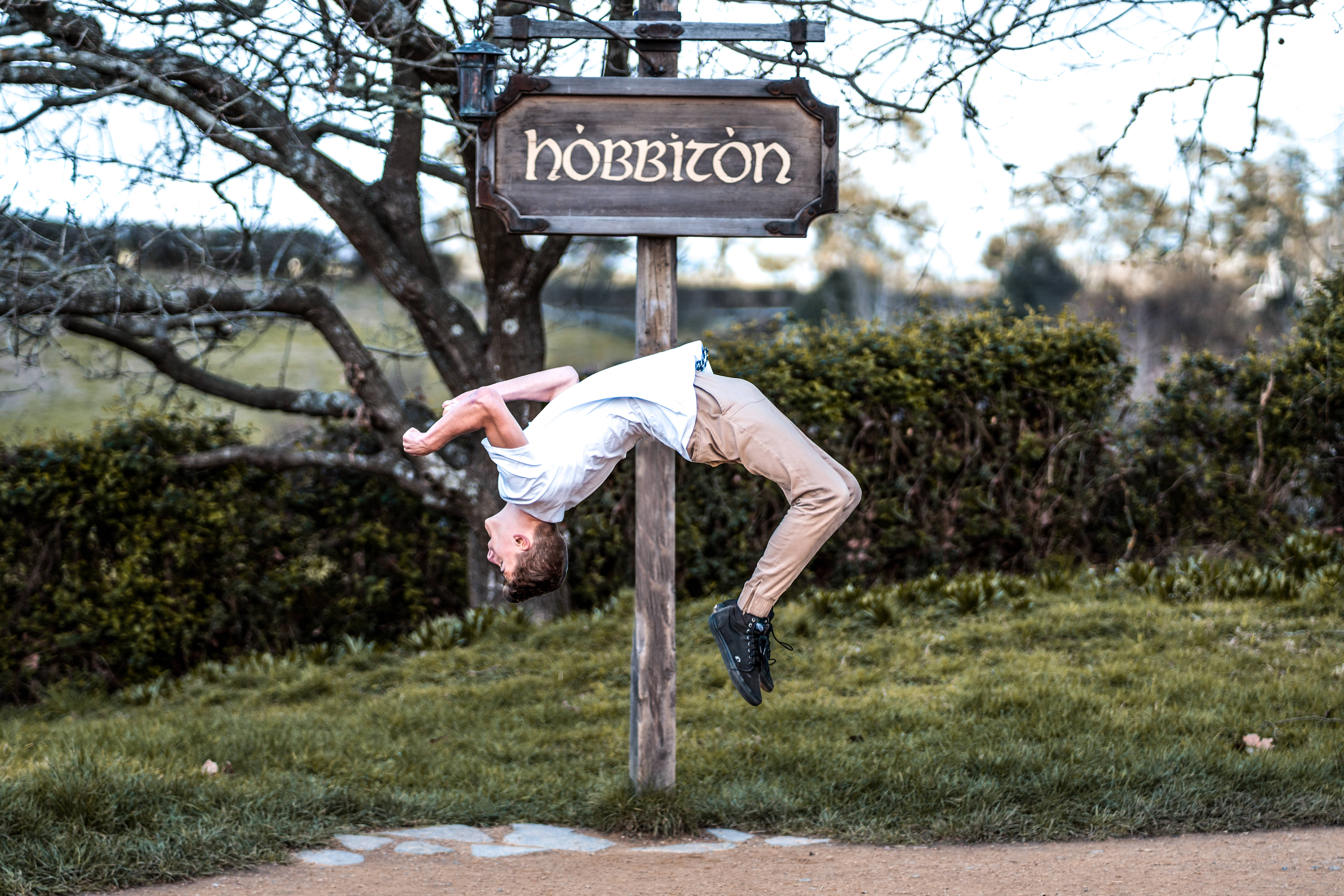 Parkour 桌布 壁紙 — 一名年輕男子在草地上的一個木製「哈比屯」標誌下凌空向後翻筋斗。