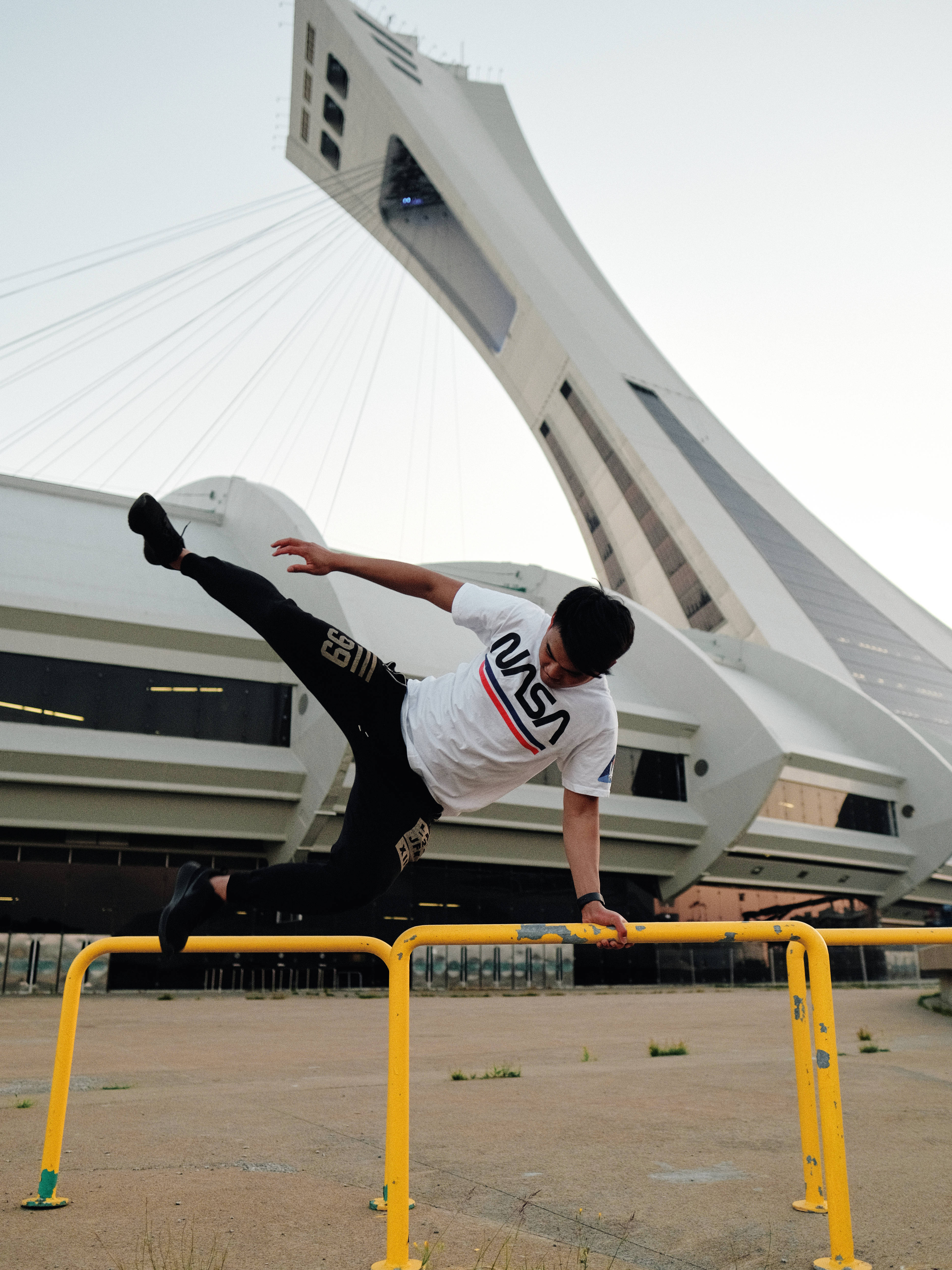 Parkour 桌布 壁紙 — 一名年輕男子在蒙特婁標誌性的傾斜塔背景下，在黃色欄杆上做出動態的跑酷動作。