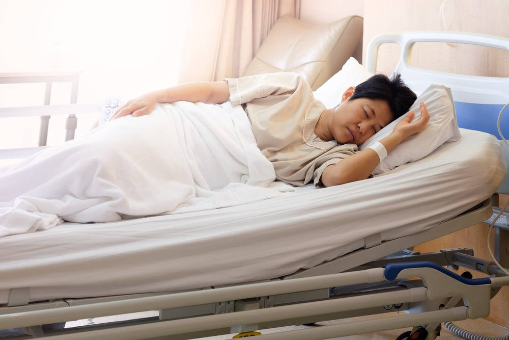 Hospital 桌布 壁紙 — 一名年輕男子在醫院的床上安詳地睡著，床上有白色床單和可見的醫療靜脈輸液管。