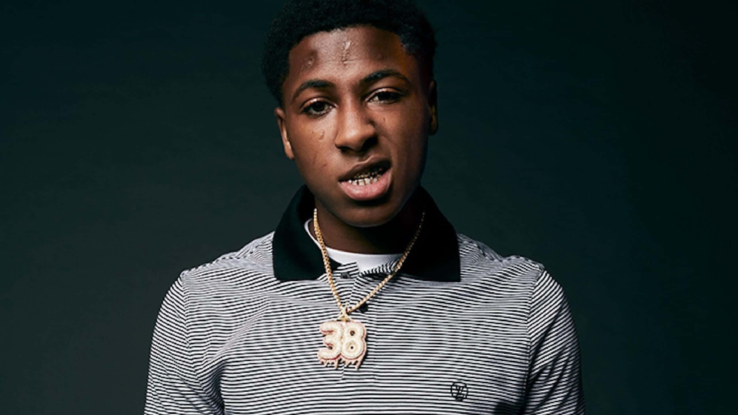 NBA YoungBoy 桌布 壁紙 — 一名年輕男子戴著一條帶有數字38的金鏈，在黑暗背景下凝視著。