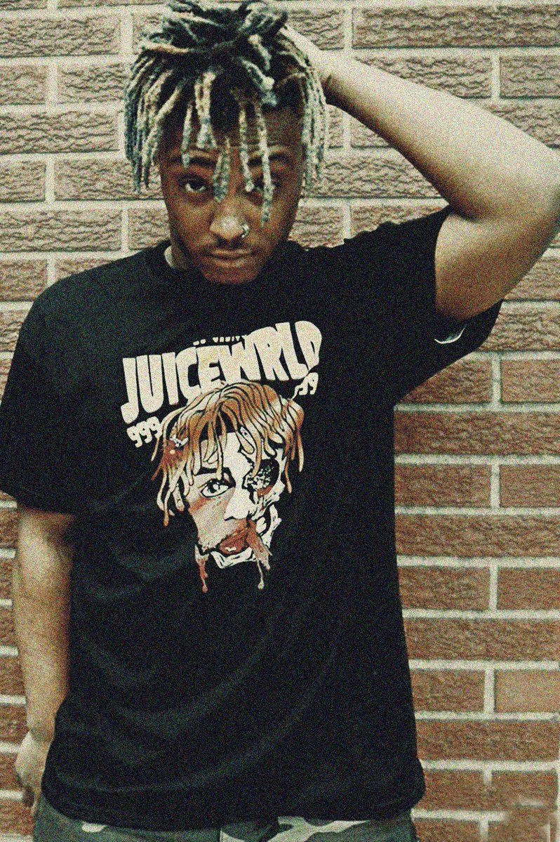 留著辮子的年輕男子身穿Juice WRLD T恤，站在磚牆前。 — Juice Wrld 壁紙