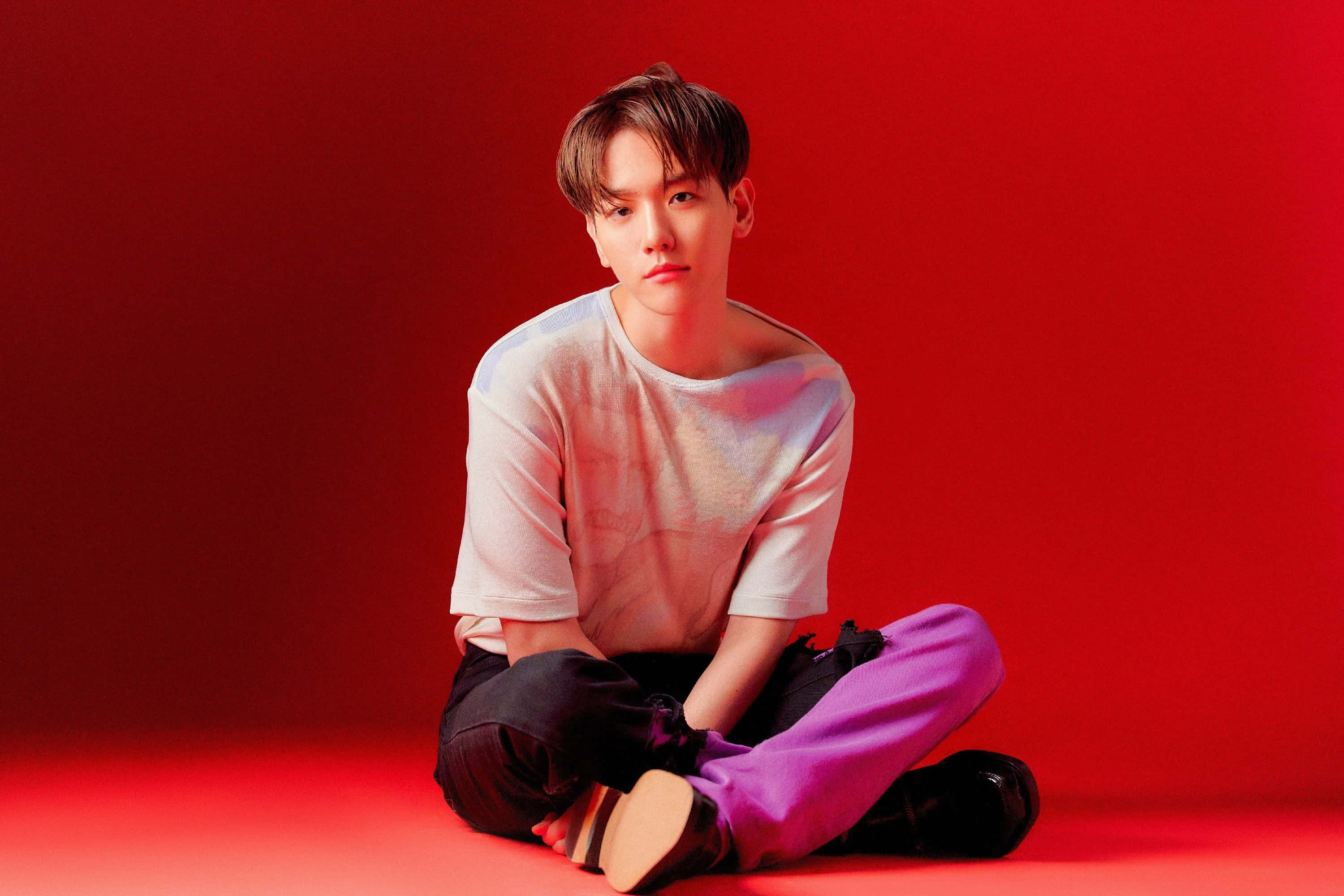 EXO 桌布 壁紙 — 一名年輕男子盤腿坐在紅色地板上，背靠相配的紅色牆壁，身穿白色襯衫和紫色褲子。