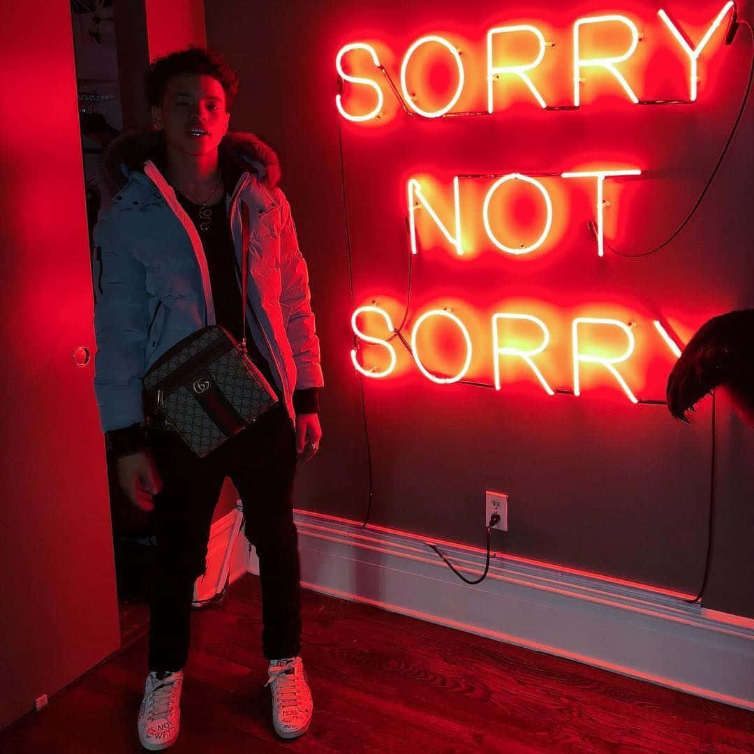 Lil Mosey 桌布 壁紙 — 一名年輕男子站在一個被牆上寫著 sorry not sorry 的紅色霓虹燈照亮的房間裡。