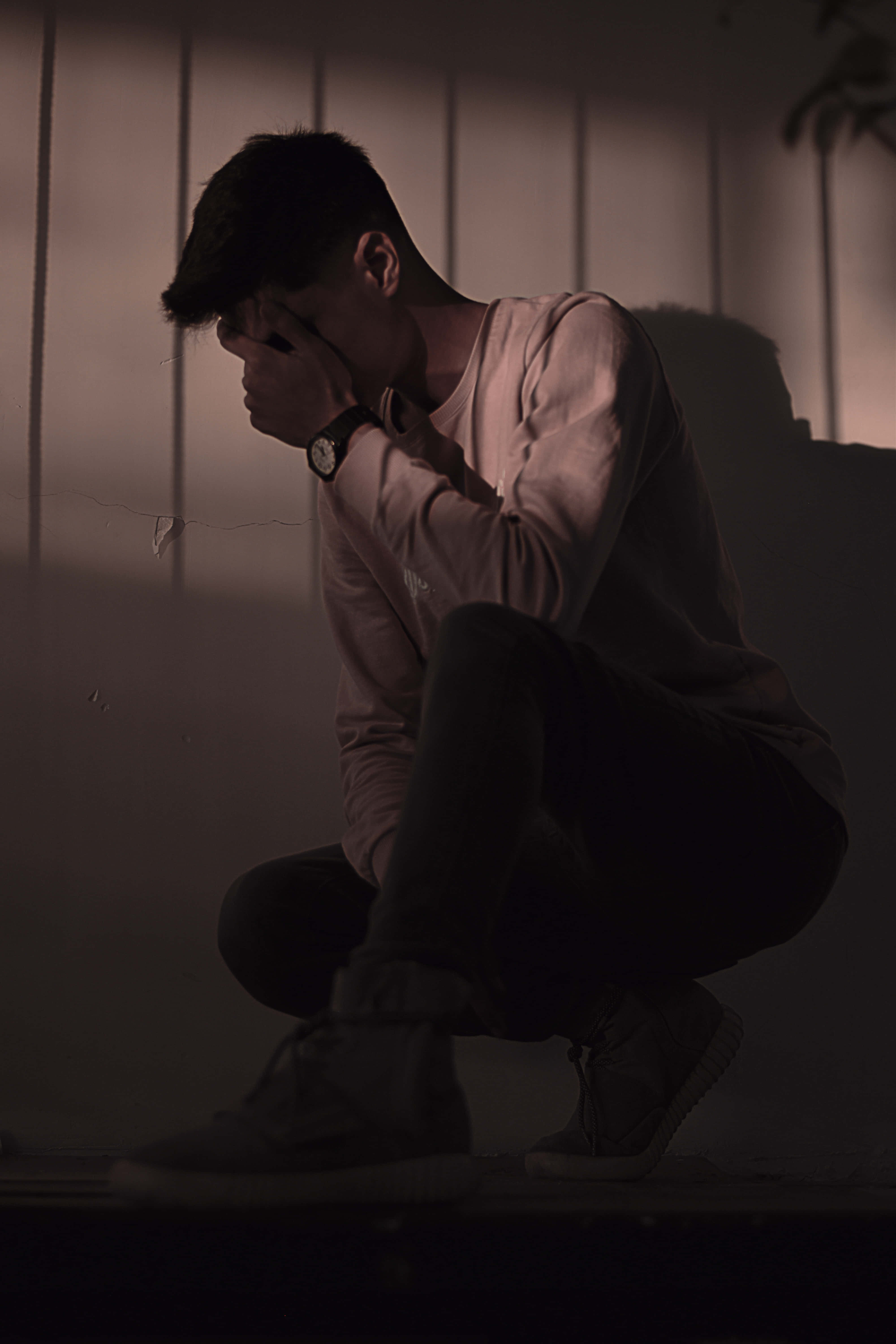 Sad Vibes 桌布 壁紙 — 一名年輕男子蹲在昏暗光線中，手掩著臉，靠著鑲板牆，處於無聲絕望的時刻。