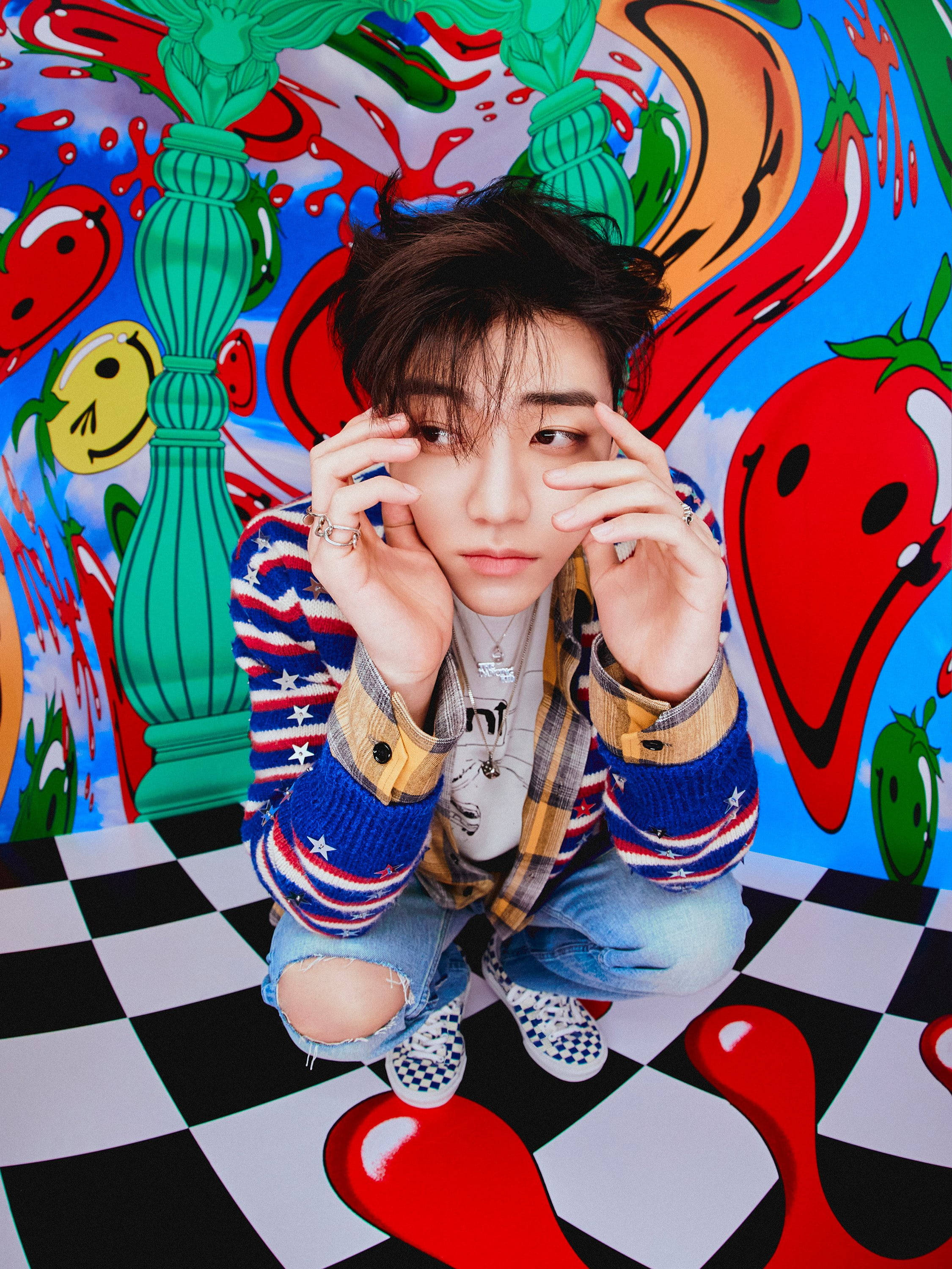jaemin 桌布 壁紙 — 一名年輕男子蹲在棋盤格地板上，背景是充滿活力的塗鴉牆，上面有卡通辣椒和柱子。