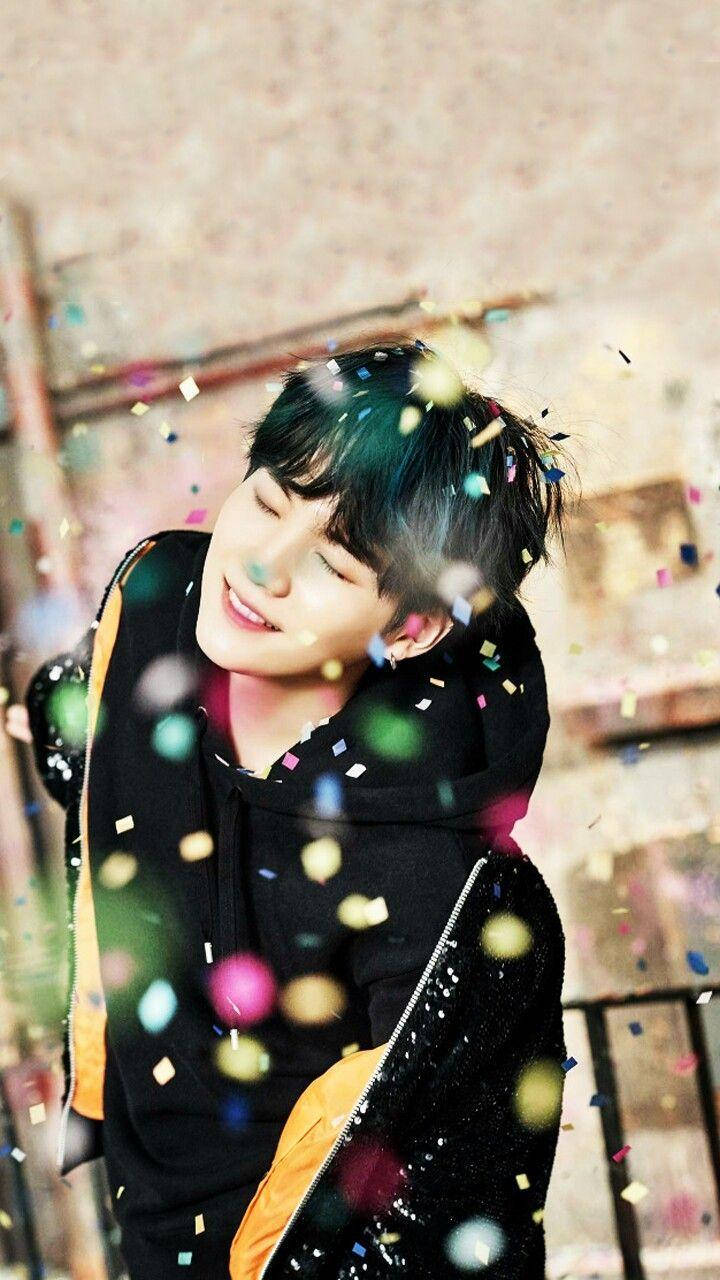 Suga Bts 桌布 壁紙 — 一名年輕男子閉上眼睛，在五彩紙屑如雨般灑落時開心地微笑。