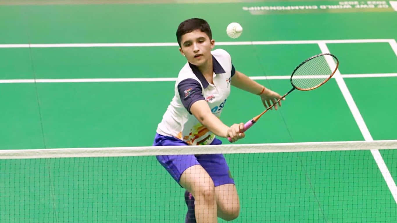 1366x768 Badminton 桌布 壁紙 — 一名年輕男羽球選手向前衝刺，在充滿活力的綠色場地上扣殺羽球。