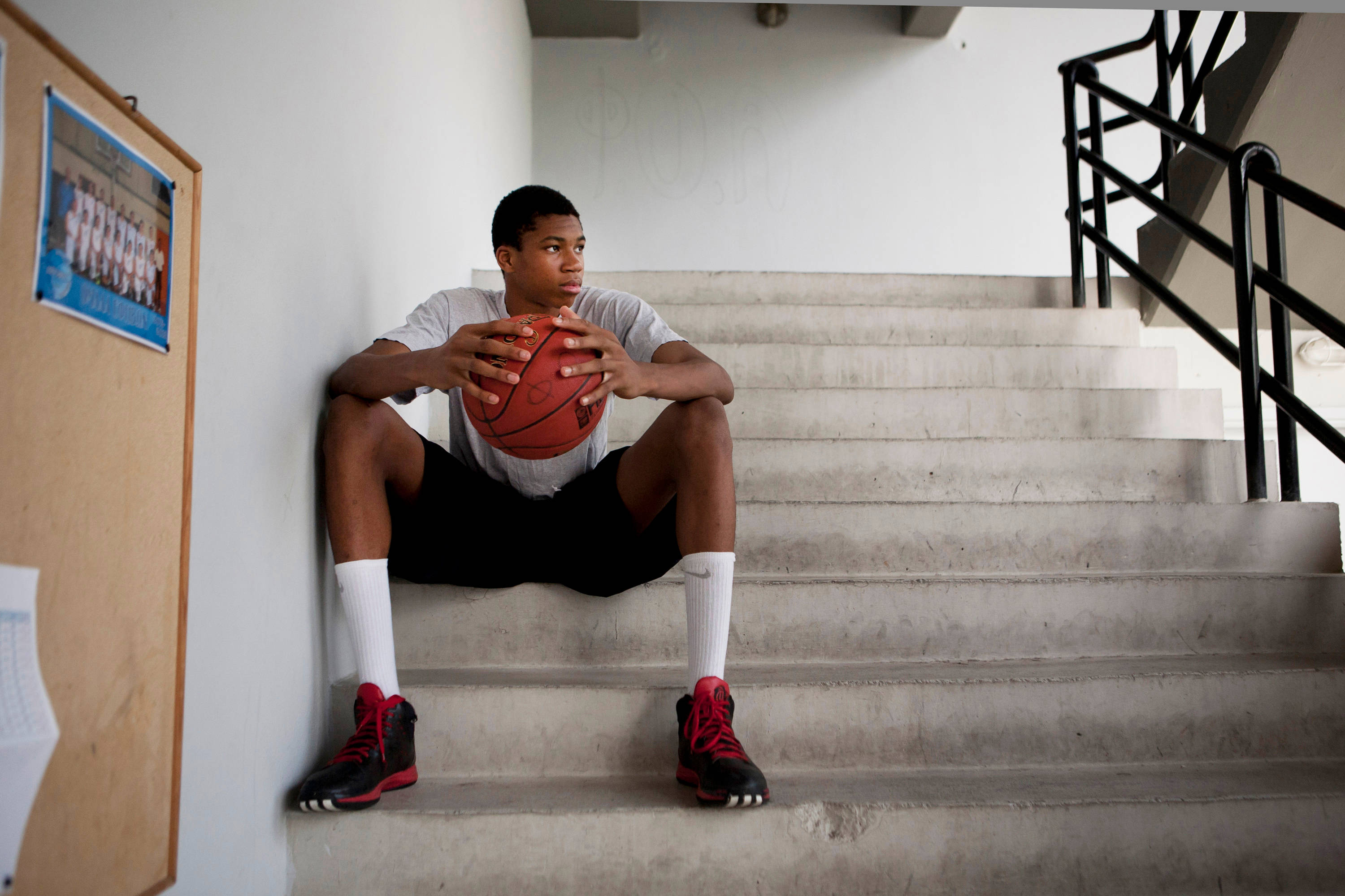 Giannis 桌布 壁紙 — 一名年輕籃球運動員坐在混凝土樓梯上，手持紅色球，穿著紅色運動鞋，望向一旁。