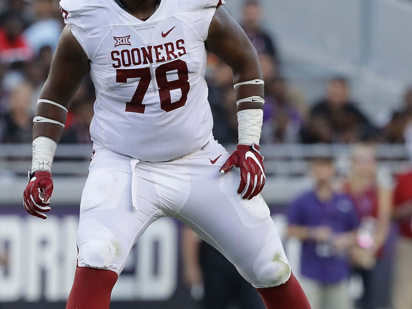 運動 桌布 壁紙 — 一名強勁的奧克拉荷馬大學 Sooners 美式足球員身穿白色與深紅色裝備，在比賽中準備就緒站在場上。