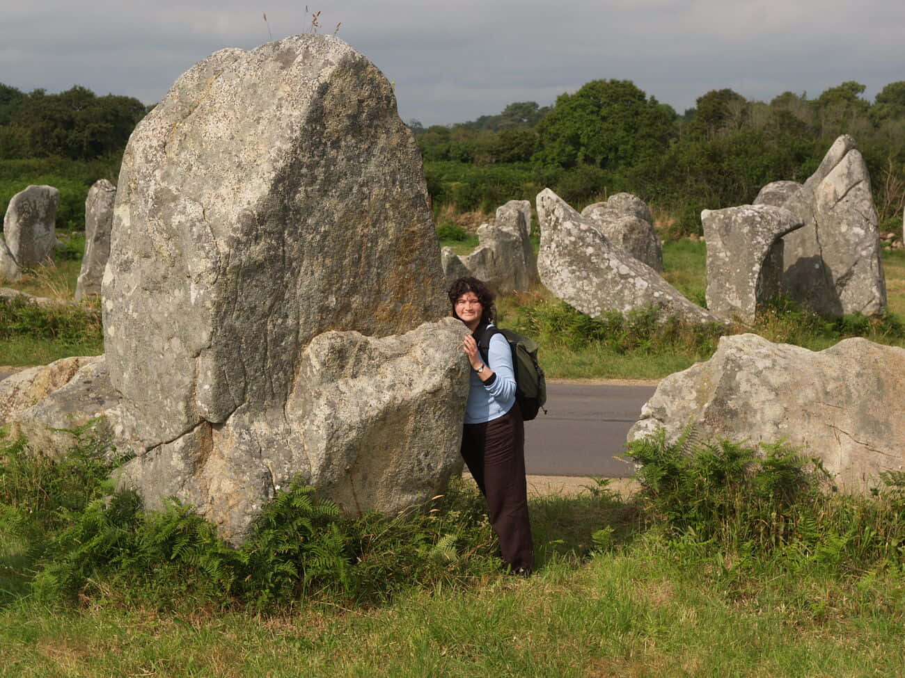 Stone 桌布 壁紙 — 一名微笑的女子靠在一塊巨大的古代立石上，四周是其他風化的巨石，天空多雲。