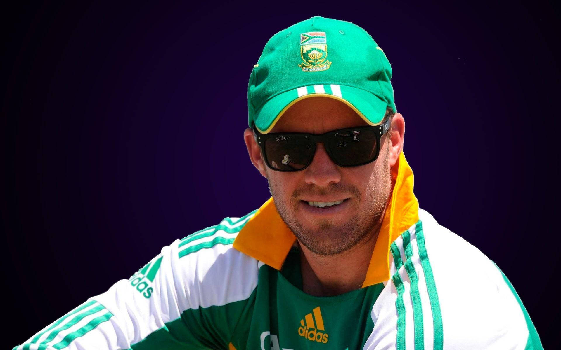 Ab De Villiers 桌布 壁紙 — 一名微笑的板球運動員身穿綠色和黃色的南非隊裝備，戴著太陽眼鏡，背景為深紫色。
