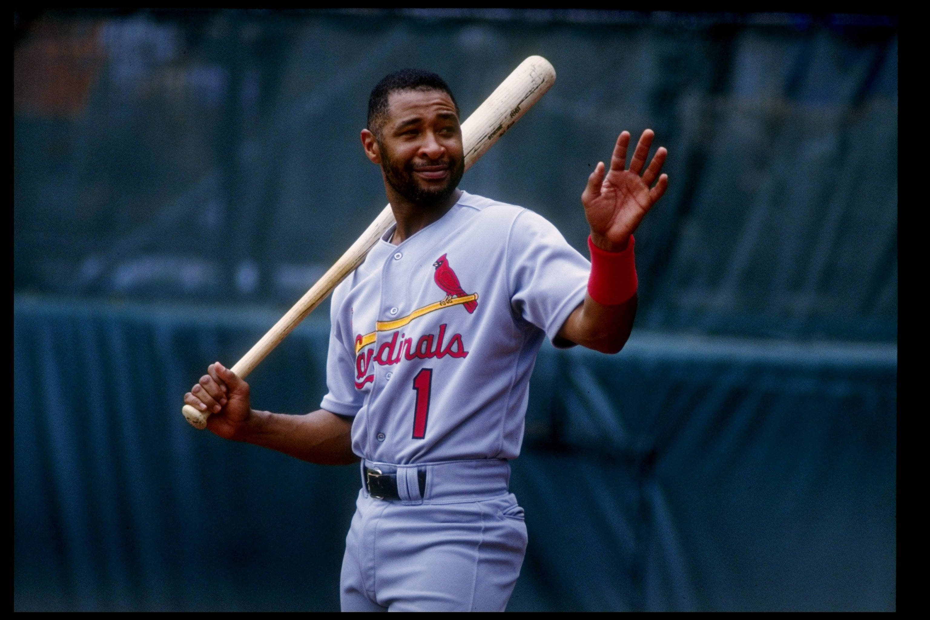 Ozzie Smith 桌布 壁紙 — 一名微笑的棒球運動員身穿紅雀隊制服，在模糊的球場背景下，將球棒扛在肩上揮手致意。