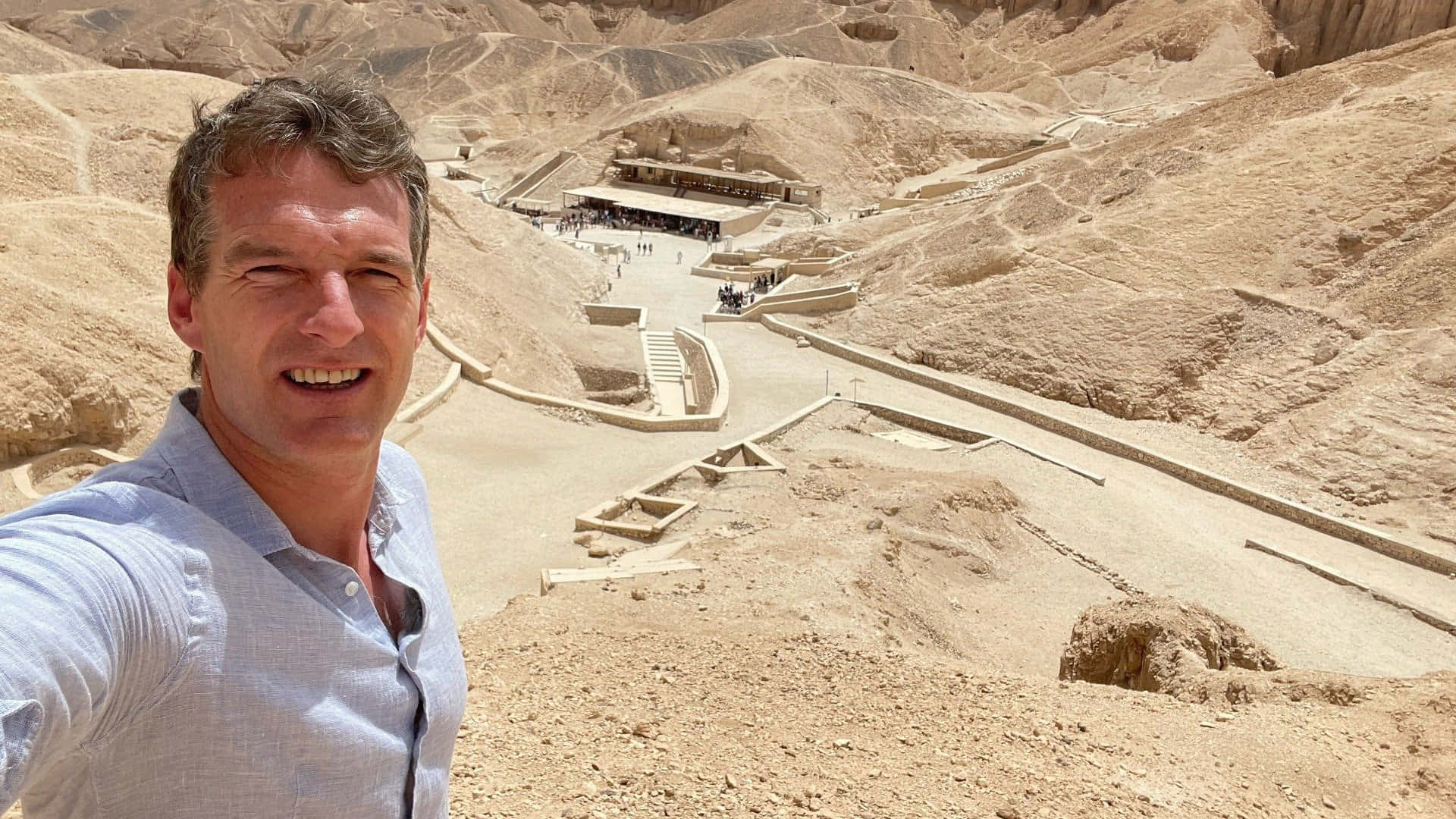 egyptian 桌布 壁紙 — 一名微笑的男子在日出時分，以金色砂岩懸崖為背景，俯瞰哈特謝普蘇特古老沙漠神廟群自拍。