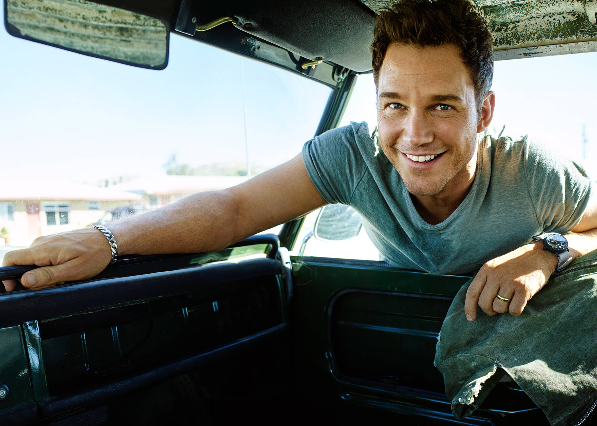 Chris Pratt 桌布 壁紙 — 一名微笑的男子在晴朗的天空下從復古車的車窗探出頭來。