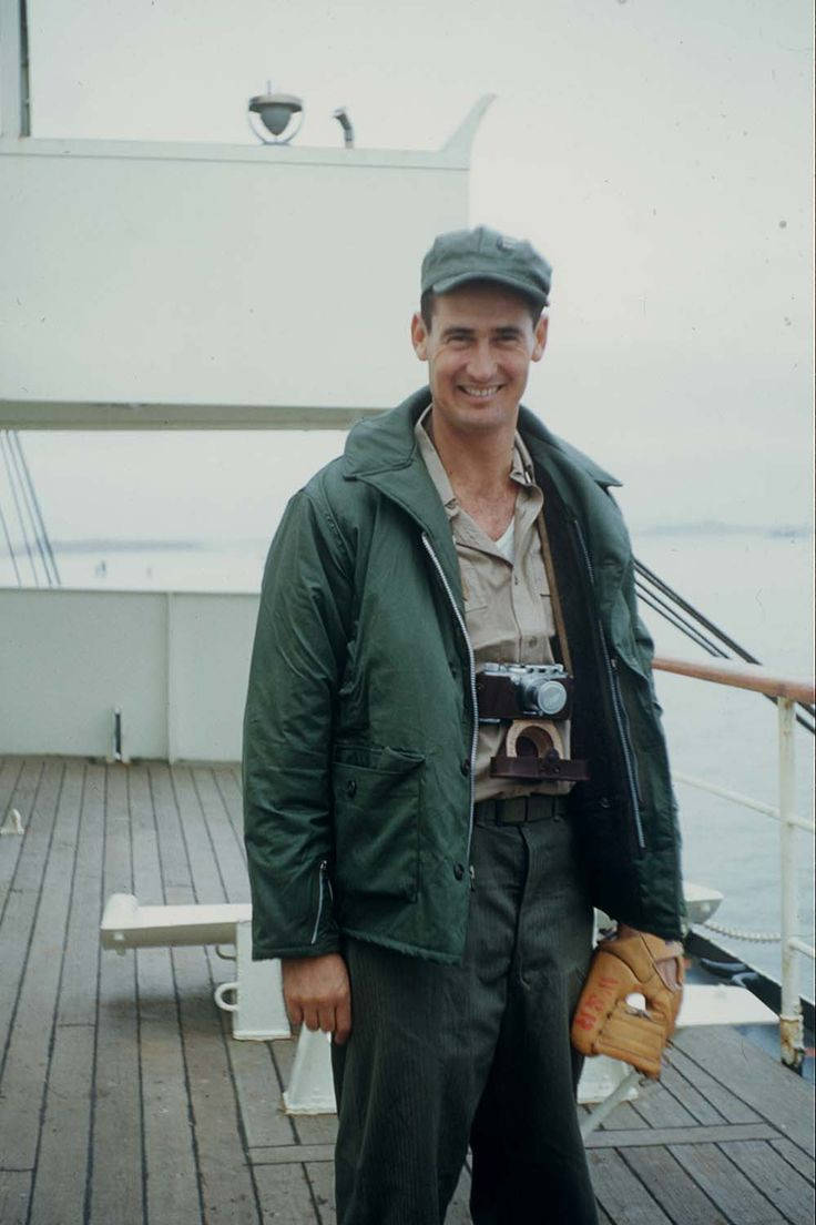 Ted Williams 桌布 壁紙 — 一名微笑的男子身穿綠色外套和帽子，站在船的木甲板上，手持相機和棒球手套。