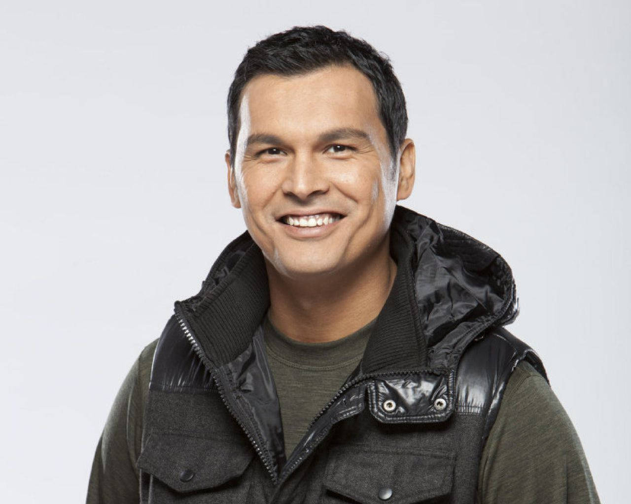 actor 桌布 壁紙 — 一名微笑的男子身穿黑色絎縫背心，內搭綠色襯衫，背景為純白色。