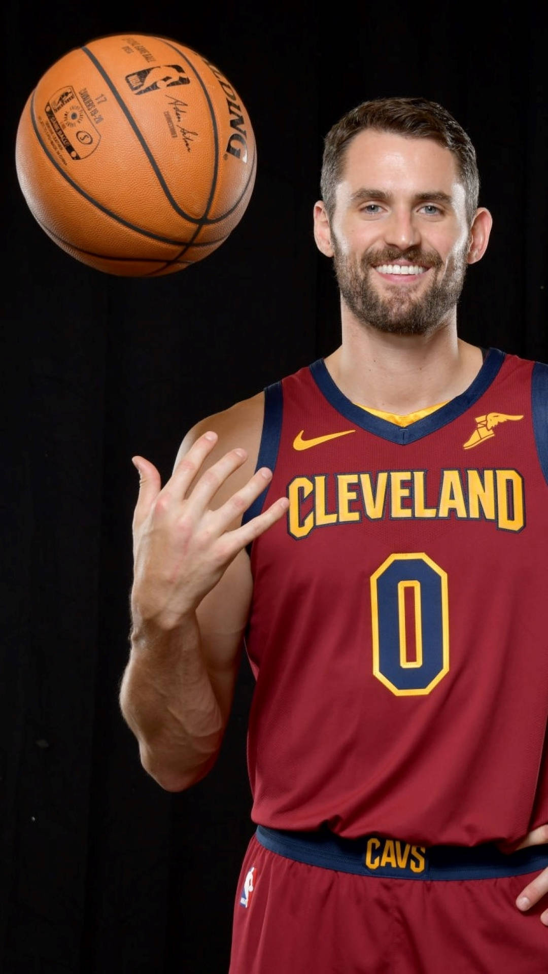 Kevin Love 桌布 壁紙 — 一名微笑的籃球運動員身穿克里夫蘭騎士隊球衣，在黑色背景前投擲籃球。