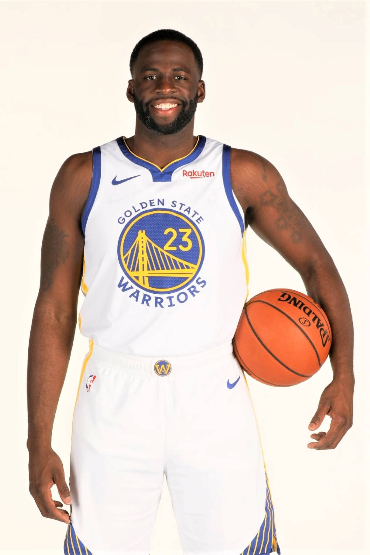 Draymond Green 桌布 壁紙 — 一名微笑的籃球運動員身穿金州勇士隊球衣，在純白色背景前手持籃球。