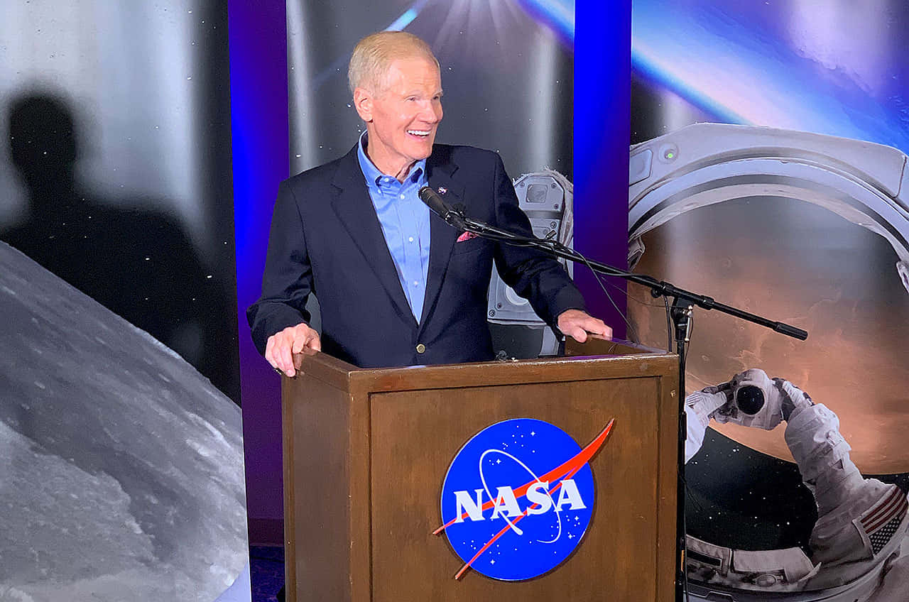 NASA 動態圖片 桌布 壁紙 — 一名微笑的西裝男子站在NASA講台上，背景是宇宙、太空人和月球。