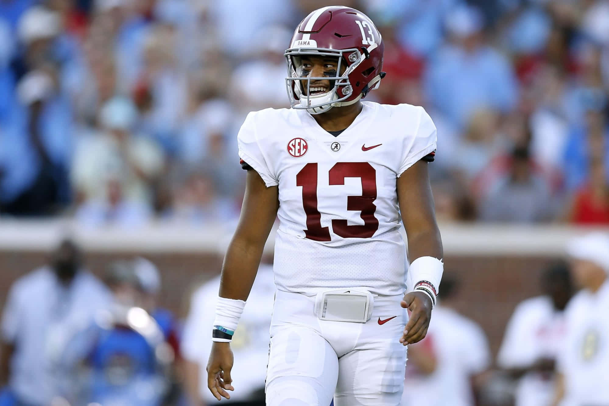Tua Tagovailoa 桌布 壁紙 — 一名微笑的阿拉巴馬美式足球四分衛，身穿白色和深紅色13號球衣，在比賽期間走進球場。