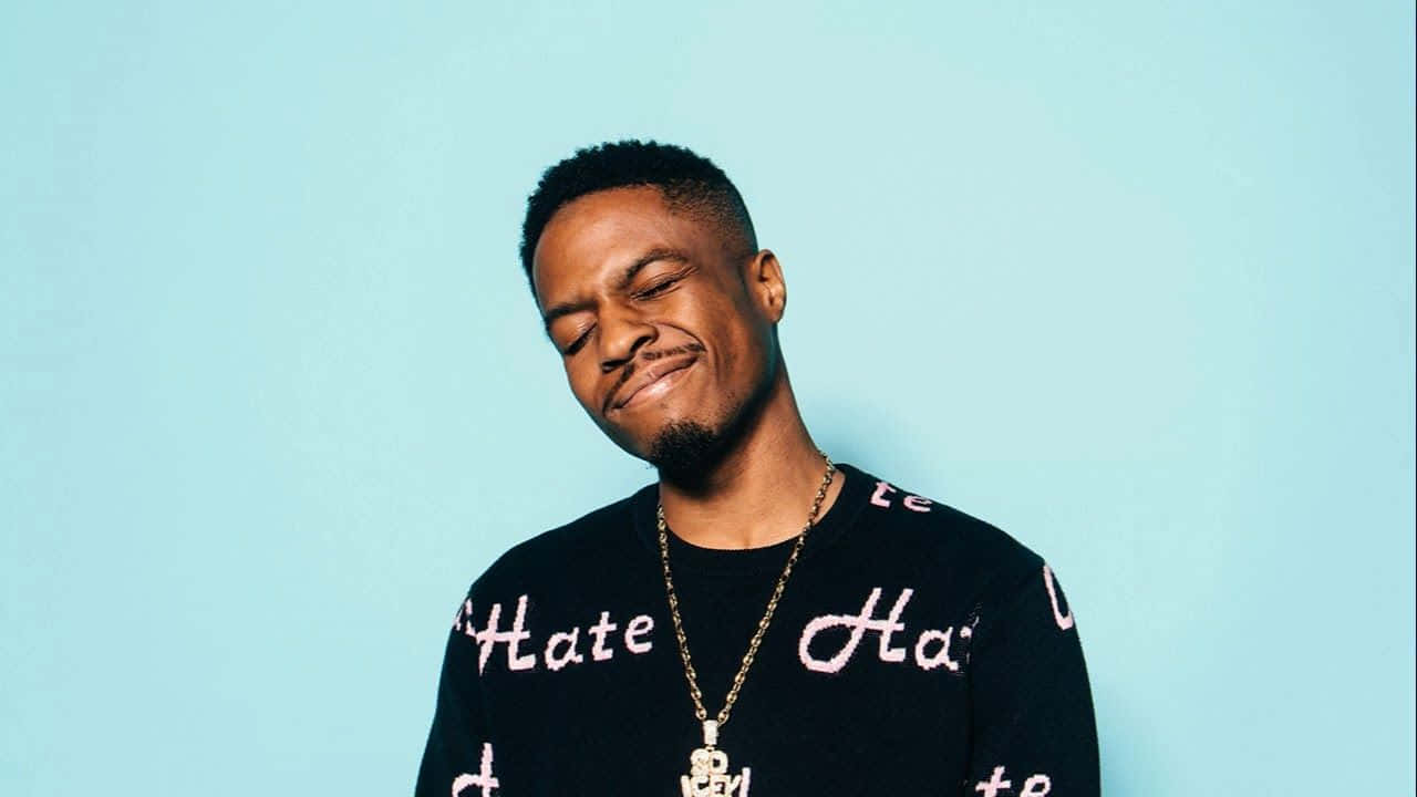 Pierre Bourne 桌布 壁紙 — 一名微笑閉眼的男子穿著黑色毛衣，上面有粉紅色 'Hate' 字樣，背景為純淺藍色。