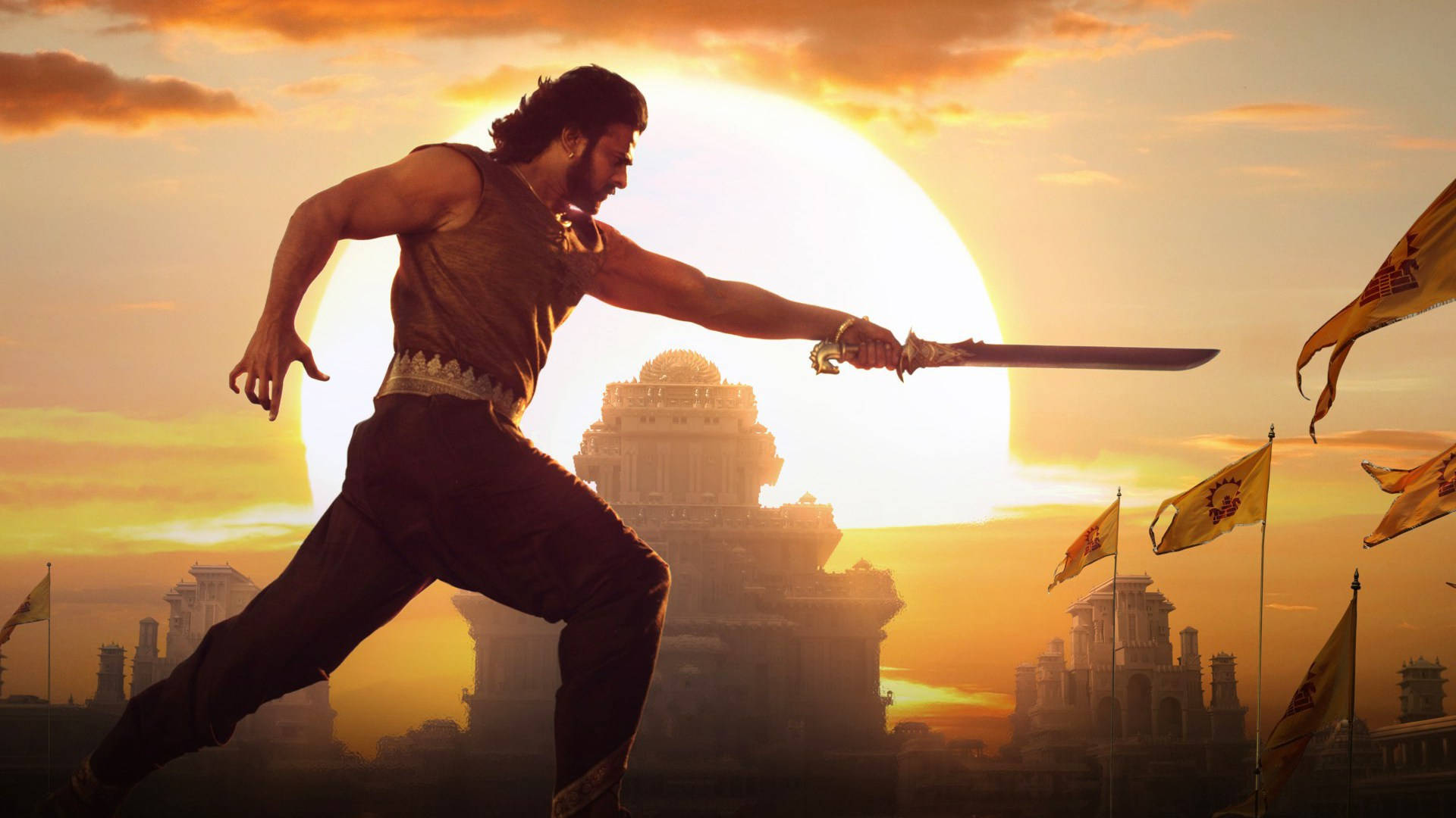 Prabhas HD 桌布 壁紙 — 一名戰士以動態姿勢揮舞劍，背景是發光的日落、古老建築和飄揚的旗幟。