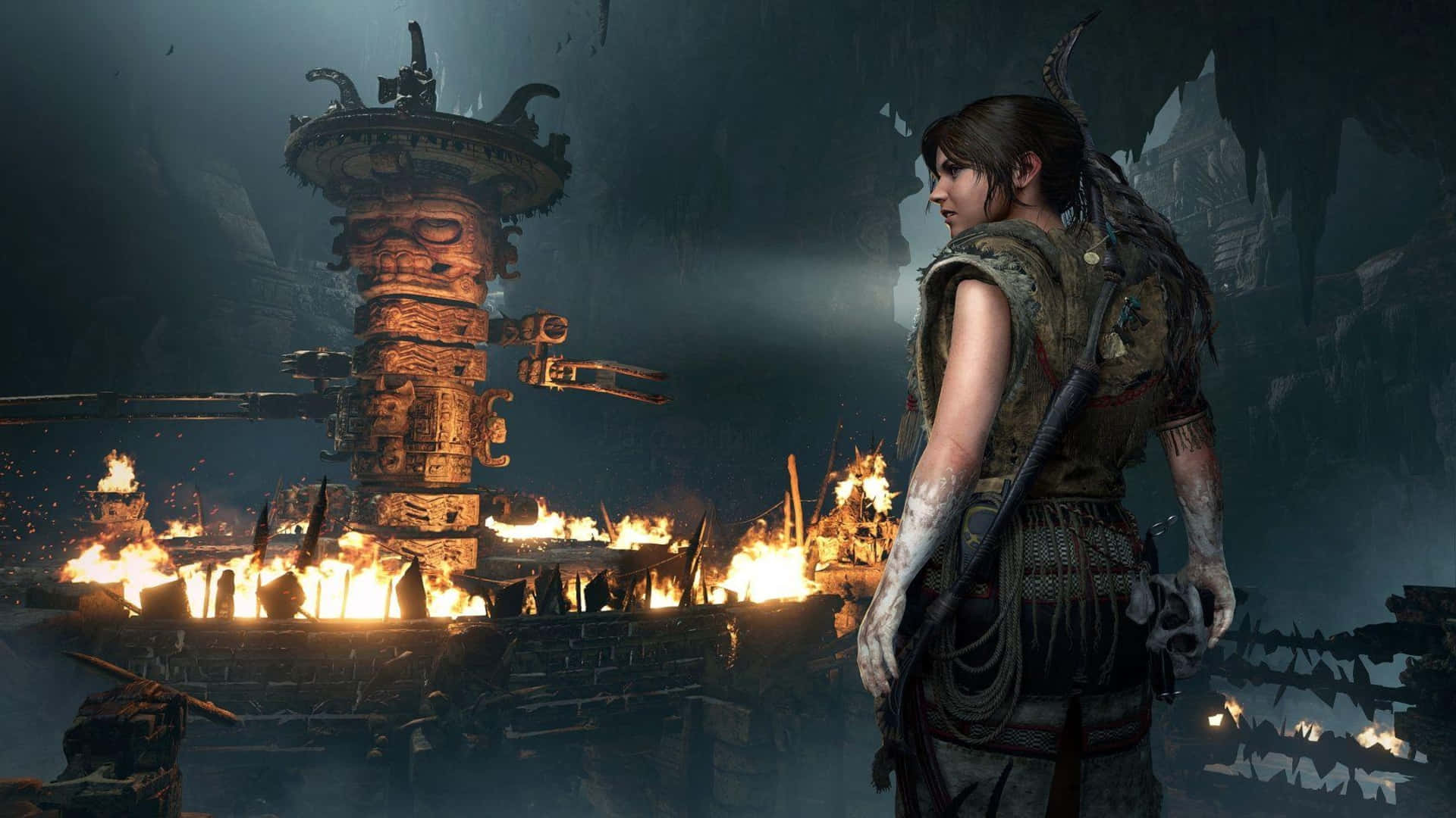 1080p Shadow Of The Tomb Raider 桌布 壁紙 — 一名戰士站在黑暗的洞穴中，古老的廢墟燃燒著猛烈的橙色火焰，照亮了石雕和滴水的鐘乳石。