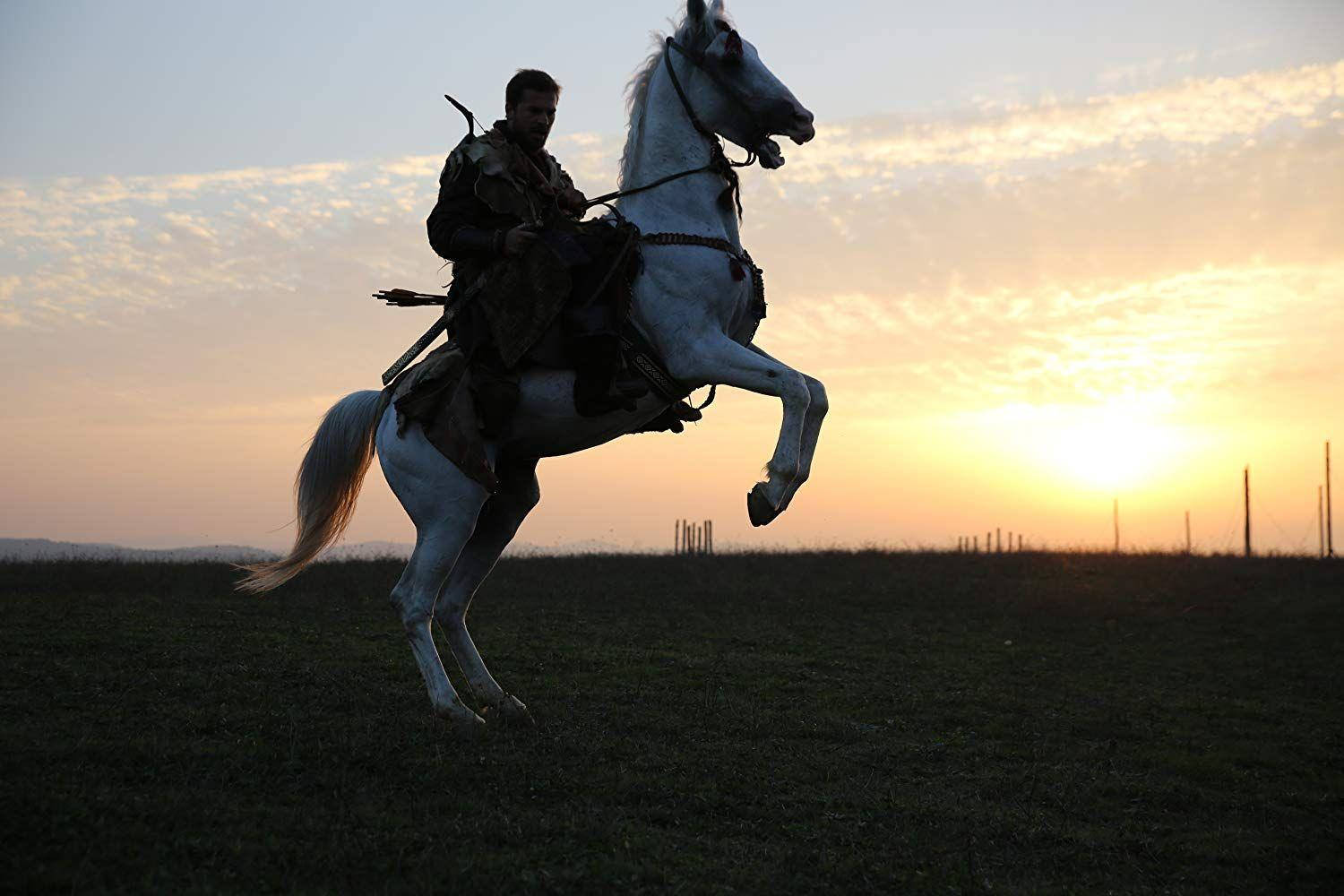Ertugrul 桌布 壁紙 — 一名戰士騎著一匹揚起前蹄的白馬，背景是草地上的金色日落。