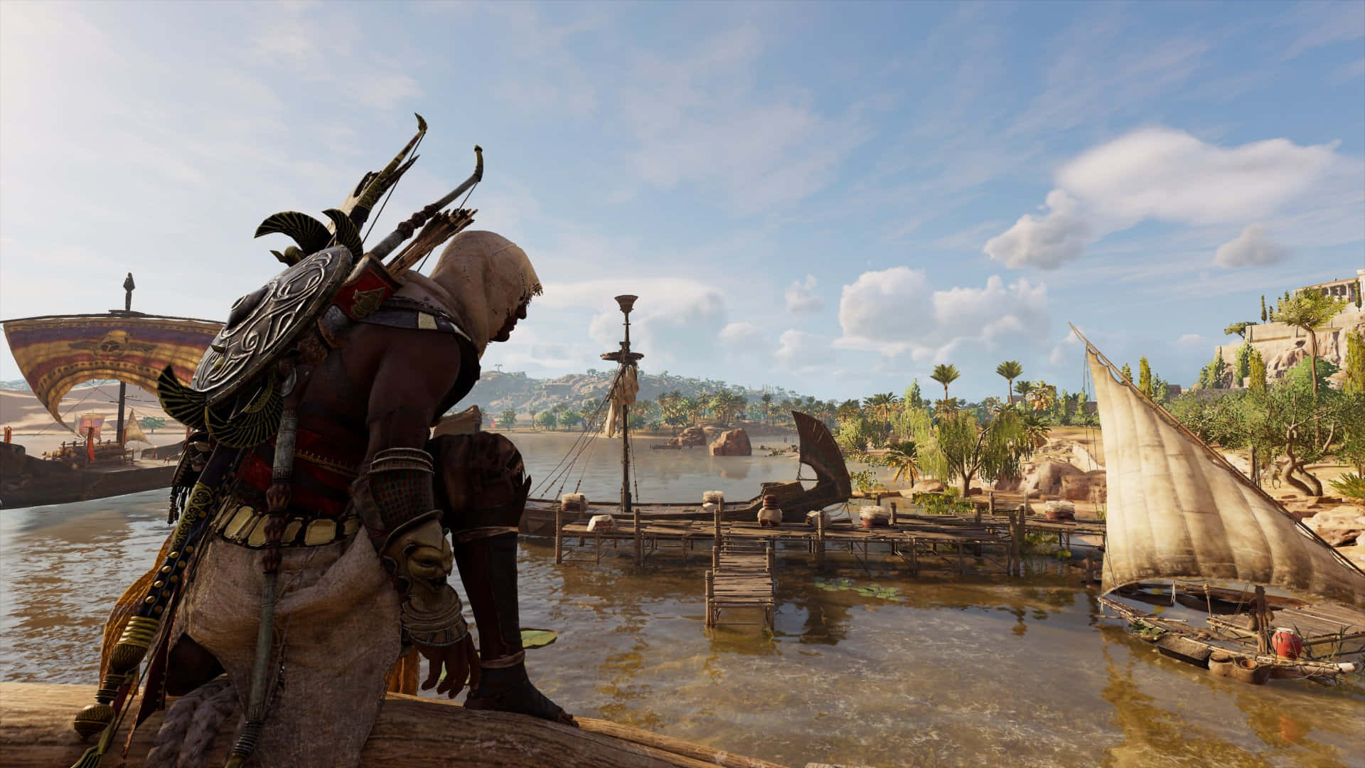 Bayek 桌布 壁紙 — 一名戴兜帽的刺客站在碼頭上，俯瞰著陽光明媚的河流，河上有帆船和古埃及風格的建築，天空蔚藍。