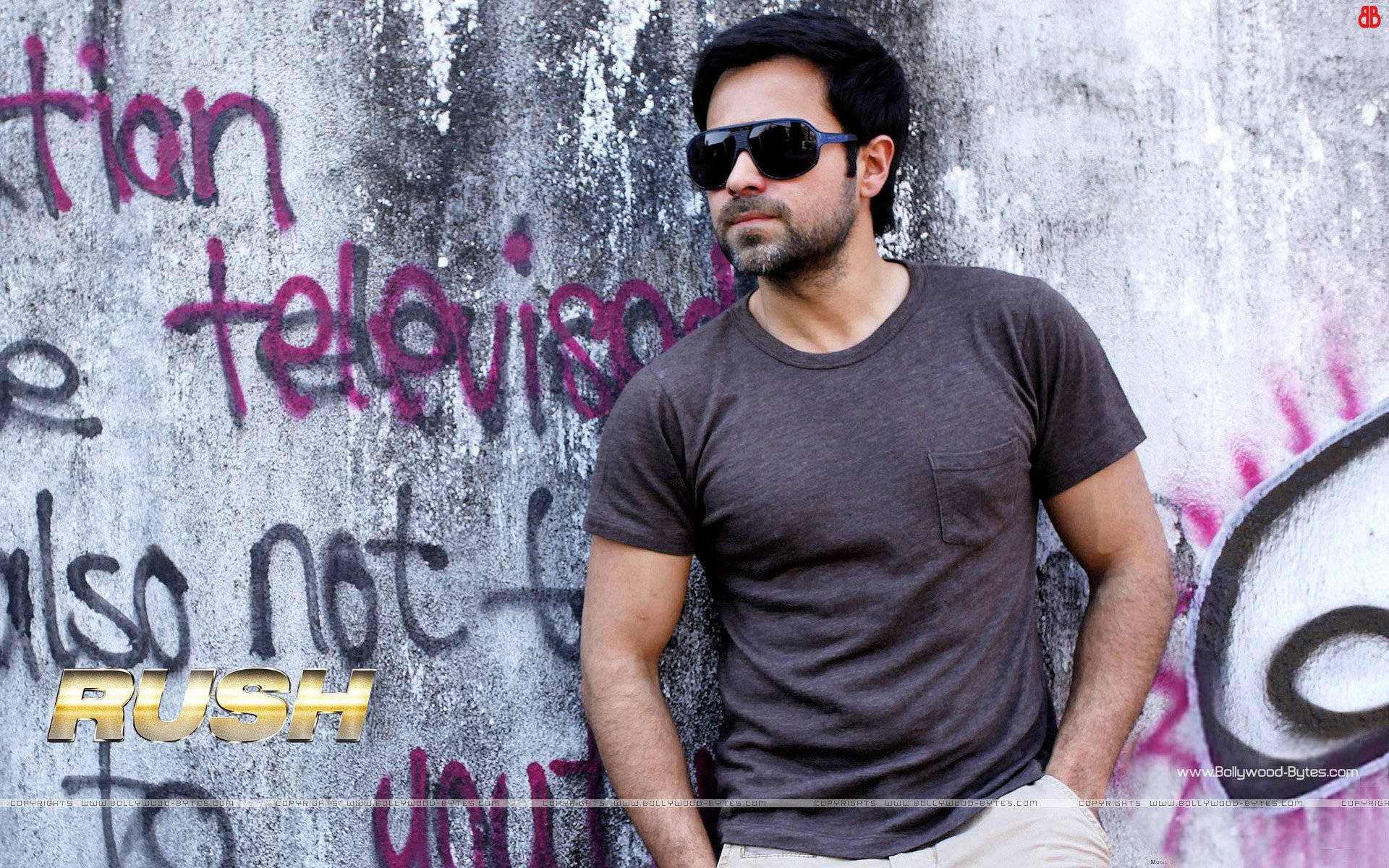 Emraan Hashmi 桌布 壁紙 — 一名戴太陽眼鏡、身穿深色T恤的男子靠在一幅塗鴉牆上，牆上有大膽的粉紅色和黑色標籤。