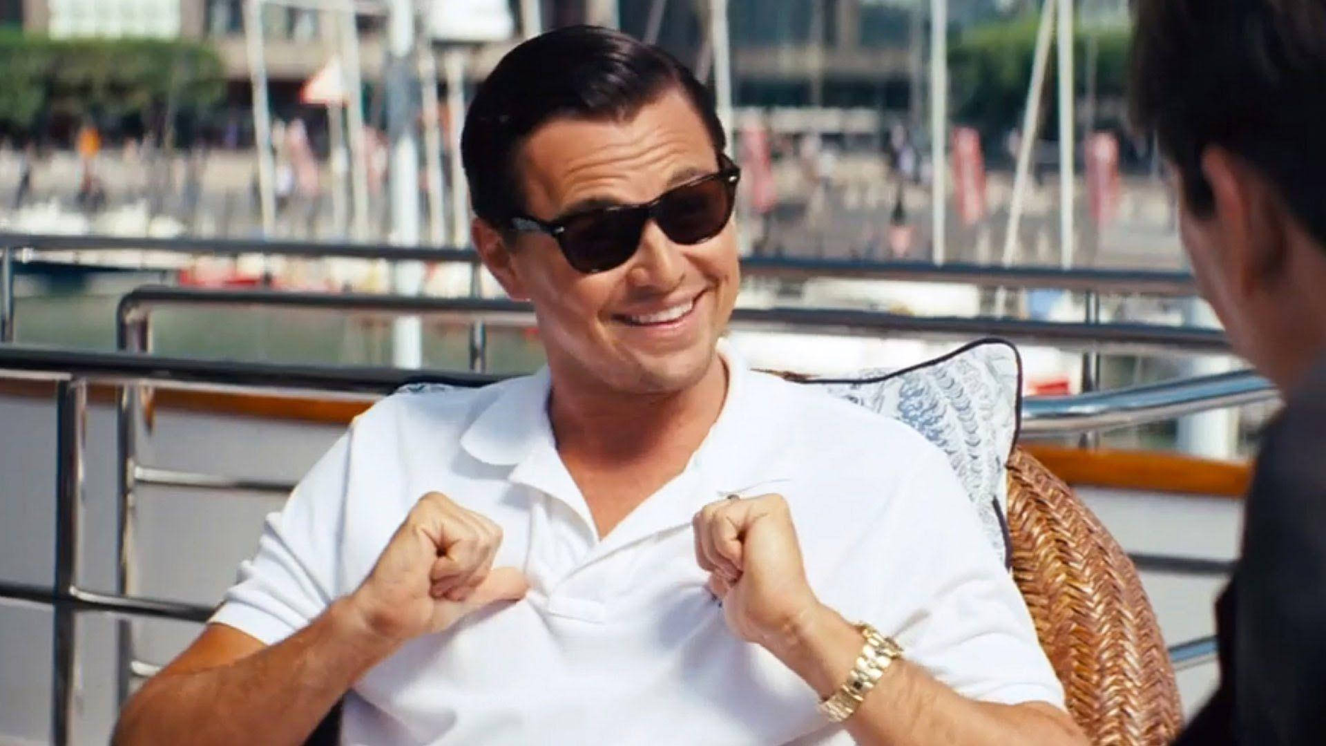 Wolf Of Wall Street 桌布 壁紙 — 一名戴太陽眼鏡、身穿白色Polo衫的男子坐在船上，背景是遊艇碼頭，自信地微笑。