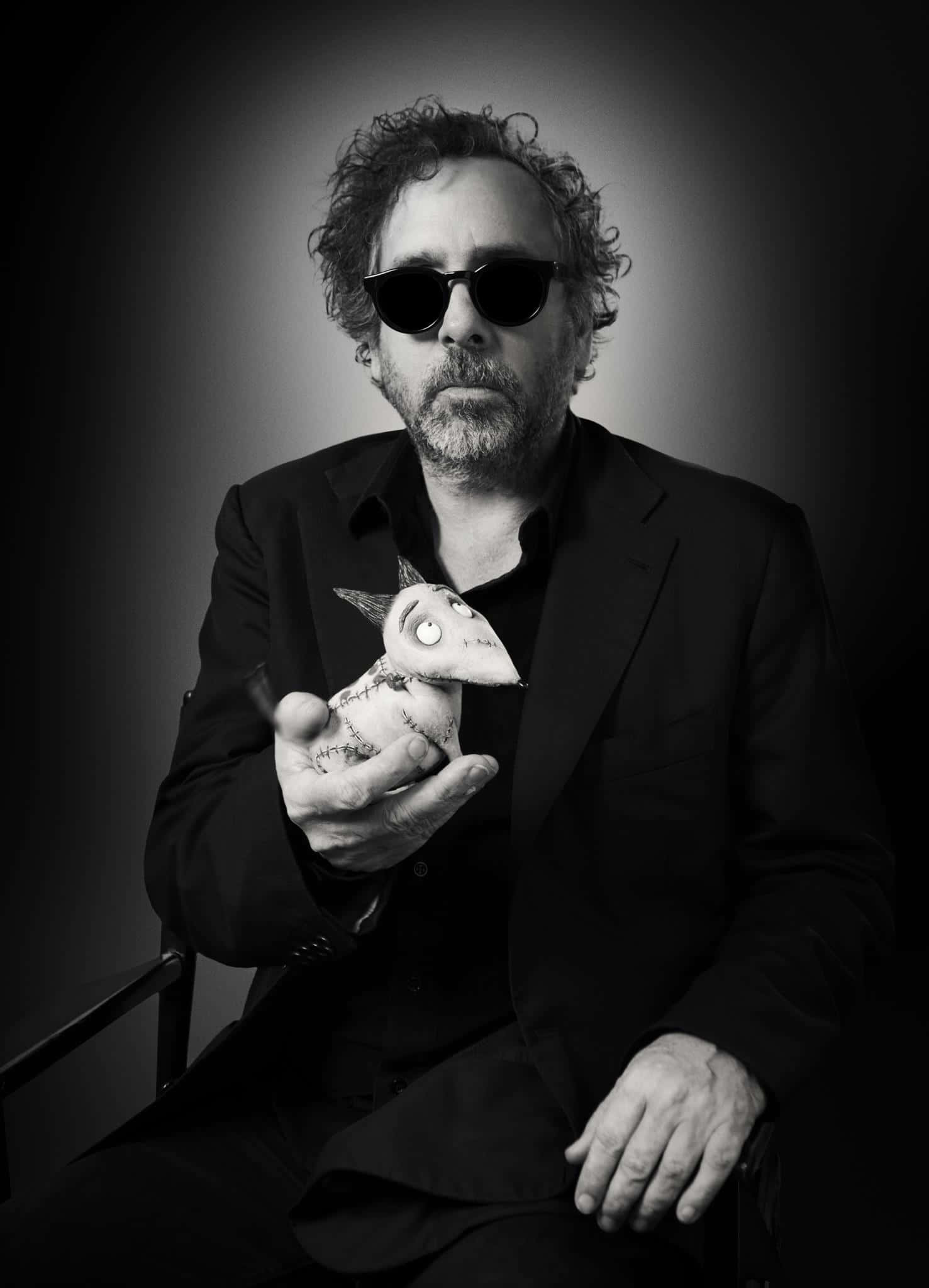tim burton 桌布 壁紙 — 一名戴太陽眼鏡的男子在深色漸變背景前拿著一個縫製的玩偶，呈現出陰鬱的黑白肖像。