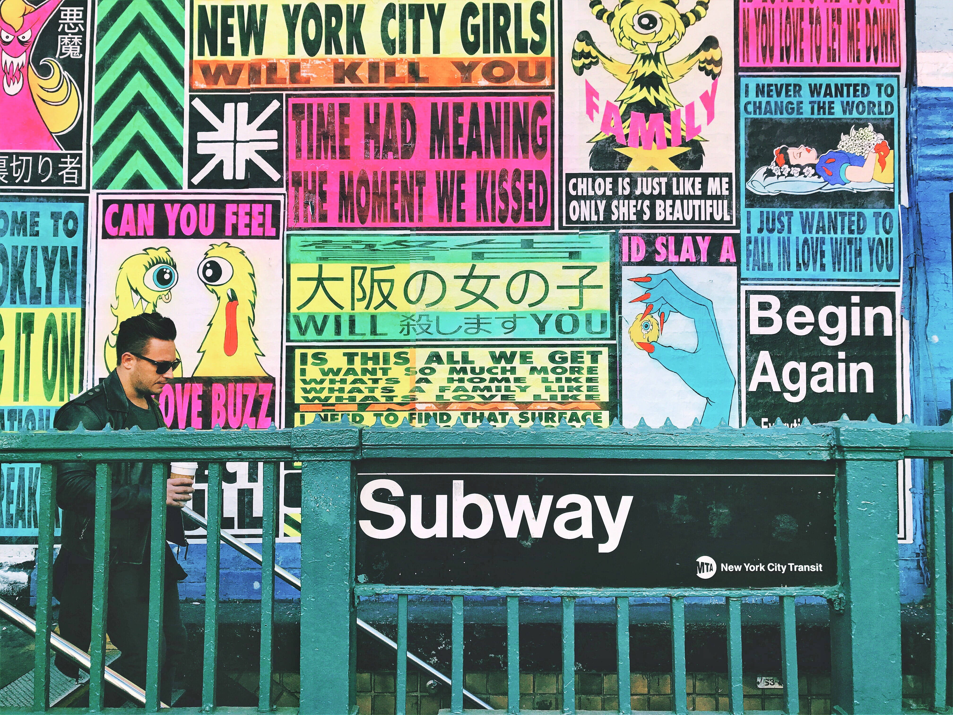 Subway 桌布 壁紙 — 一名戴太陽眼鏡的男子在紐約市一個綠色地鐵入口附近走過一面充滿色彩繽紛塗鴉海報的牆壁。