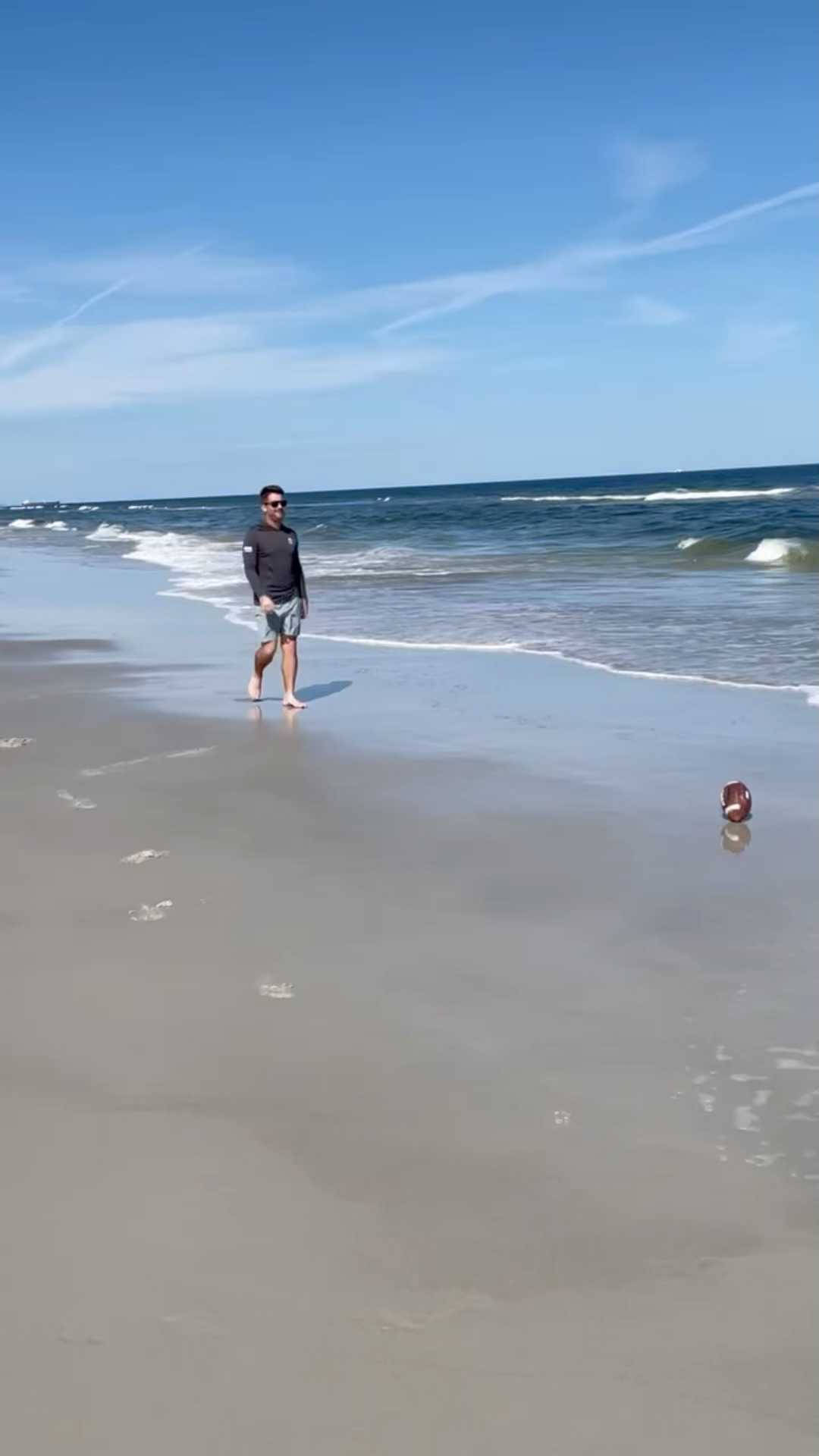 夏天 桌布 壁紙 — 一名戴太陽眼鏡的男子赤腳走在濕沙上，溫柔的海浪在晴朗的藍天下翻滾。