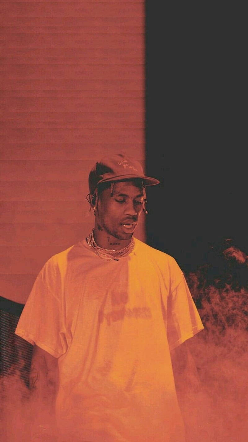 Travis Scott Aesthetic 桌布 壁紙 — 一名戴帽子和黃色襯衫的男子站在煙霧瀰漫的紅光中，靠著條紋牆壁，閉著眼睛，營造出一個充滿氛圍的表演時刻。