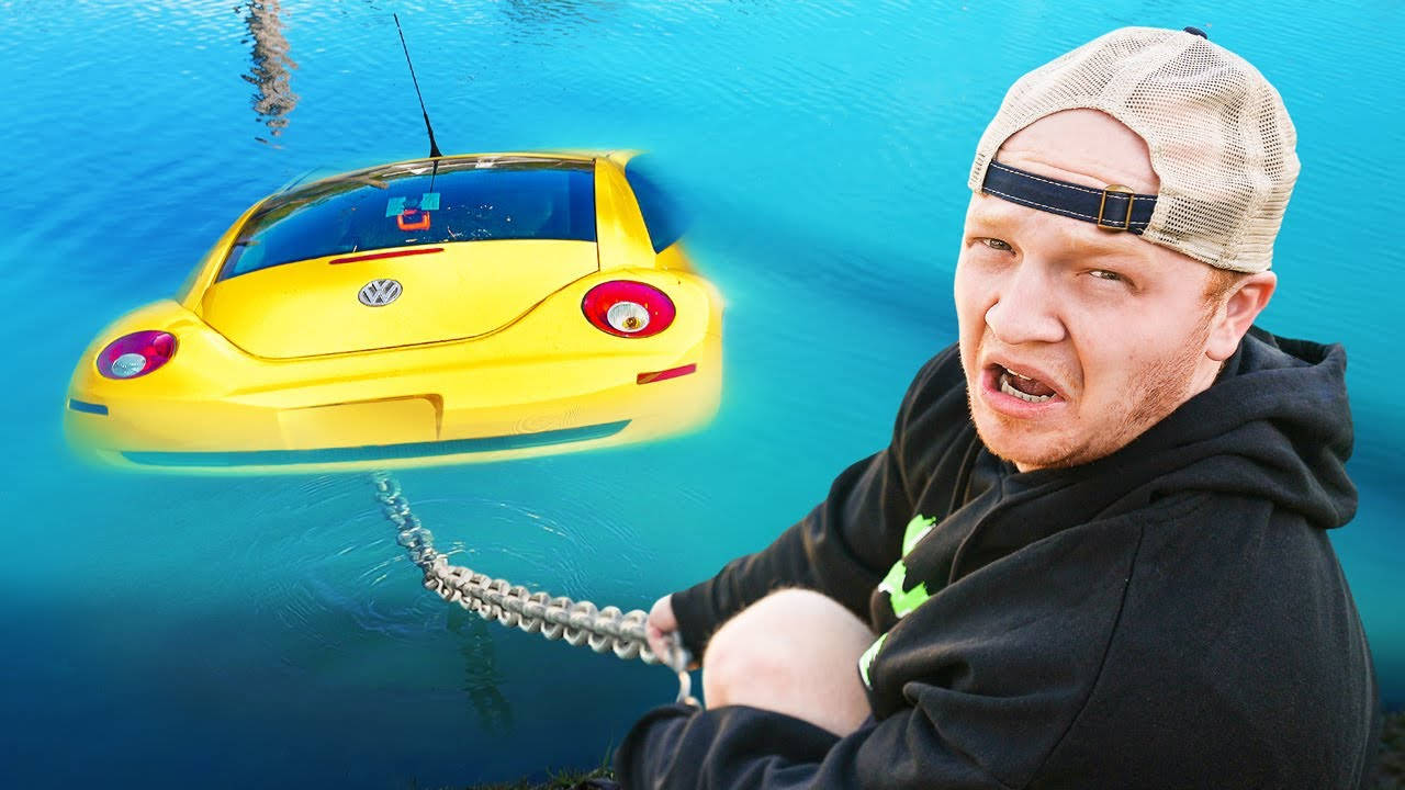 Unspeakable 桌布 壁紙 — 一名戴帽子的男子正用力用鏈條將一輛黃色福斯金龜車從藍綠色水中拉出。