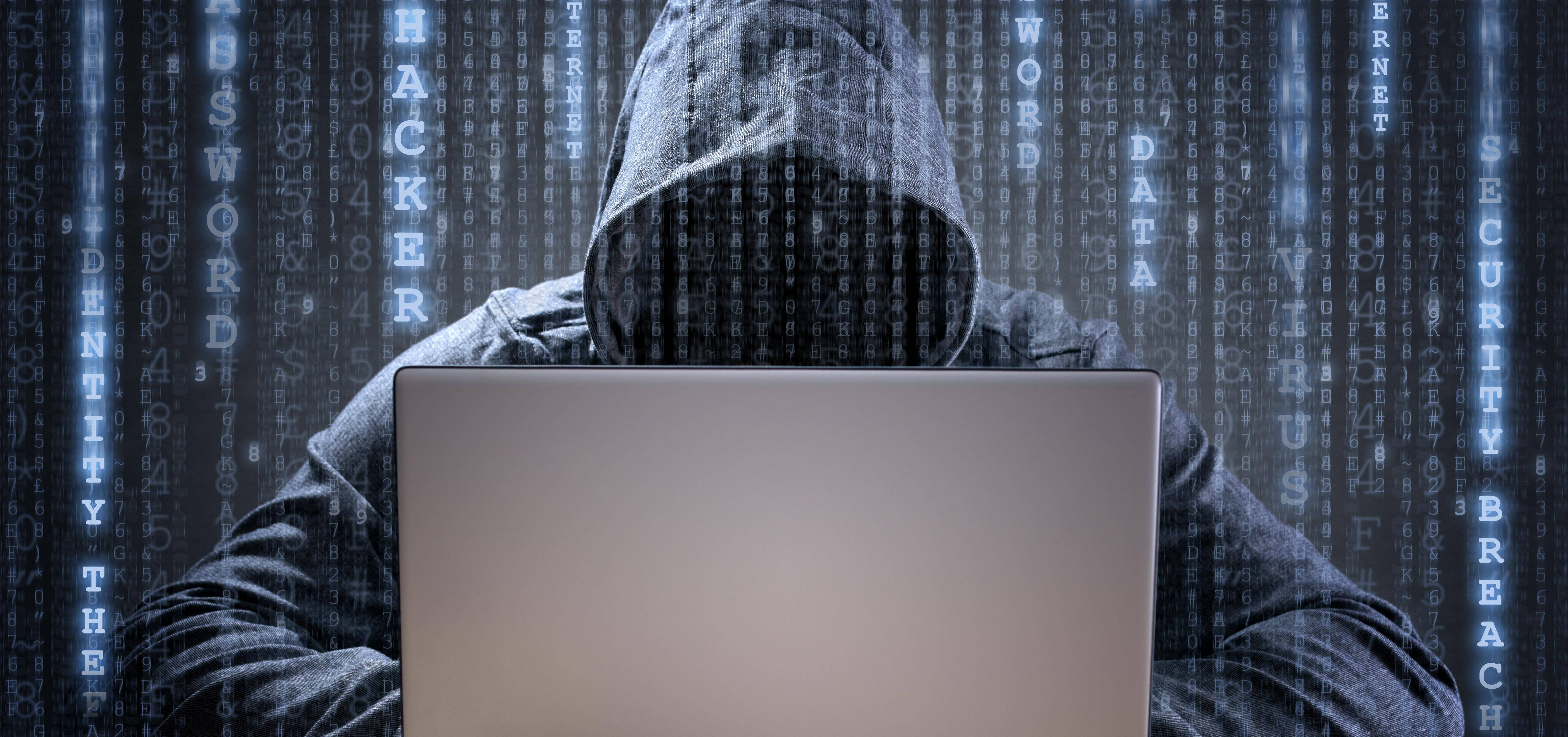 security 桌布 壁紙 — 一名戴帽的黑客坐在筆記型電腦前，數位代碼在黑暗的賽博龐克環境中環繞著他們。
