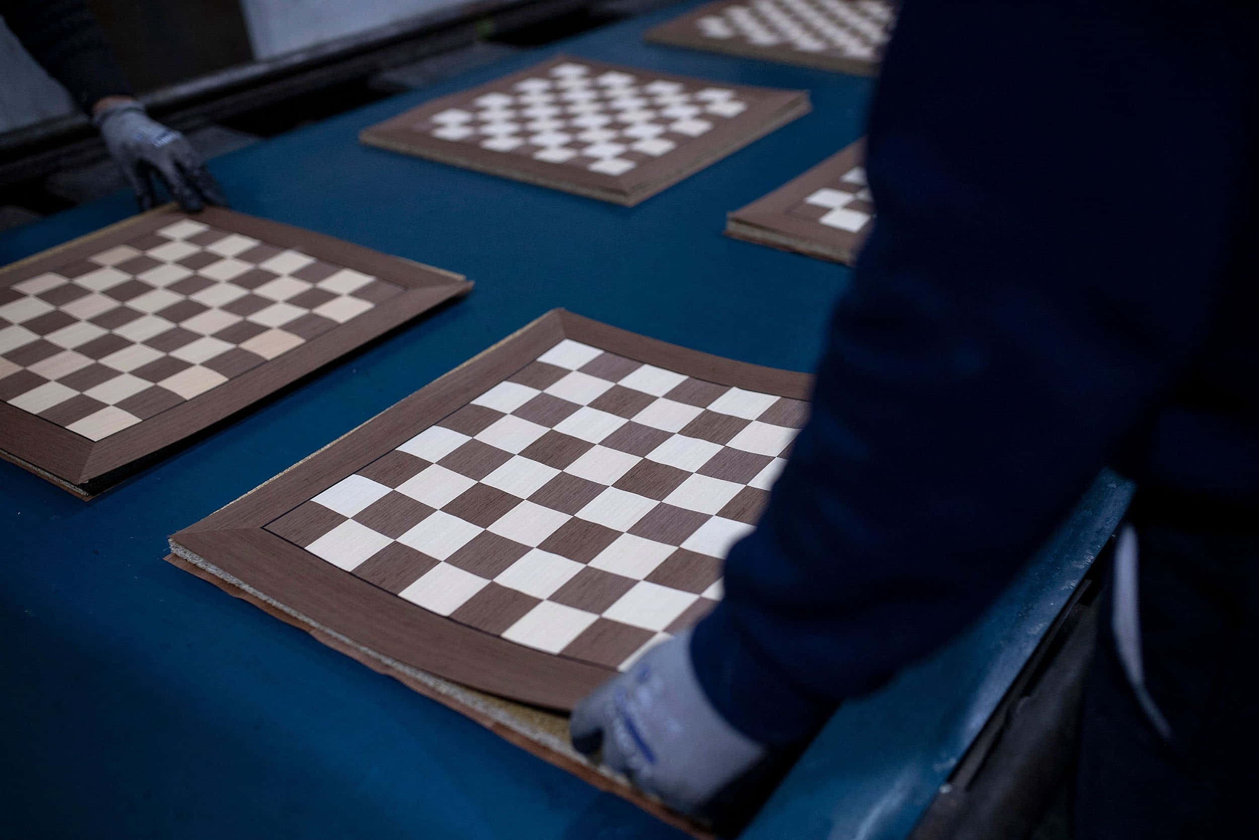 Chessboard 桌布 壁紙 — 一名戴手套的工人在工廠環境中的藍色輸送帶上組裝木製棋盤。