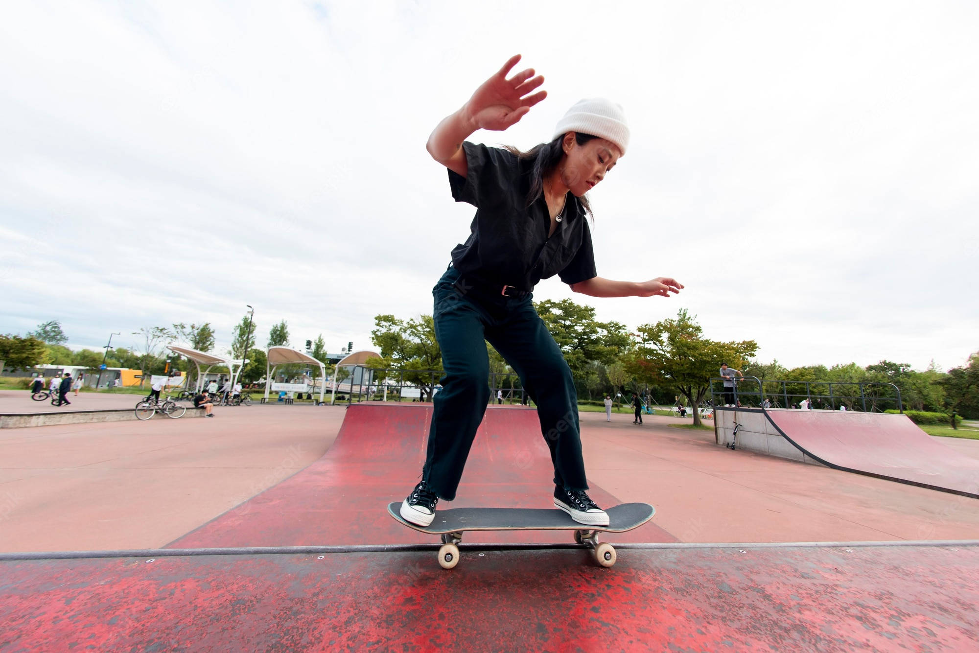 skateboarding 桌布 壁紙 — 一名戴白色冷帽、穿黑色衣服的滑板手在多雲的天空下，於戶外滑板公園的紅色坡道上動態平衡。