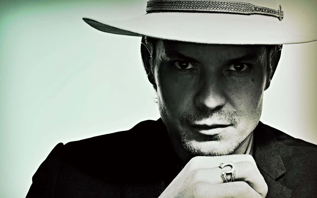 timothy olyphant 桌布 壁紙 — 一名戴白色帽子和深色西裝的男子，舉起的手上戴著銀戒指，在柔和的綠色漸變背景前凝視著。