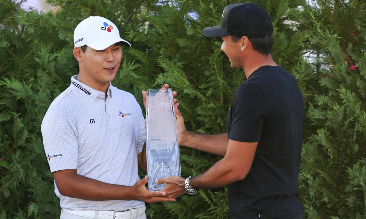 Trophy 桌布 壁紙 — 一名戴白色帽子和穿白色襯衫的高爾夫球手，在綠色灌木叢的背景下，從另一名戴黑色帽子和穿黑色襯衫的男子手中接過一個高大的透明獎盃。