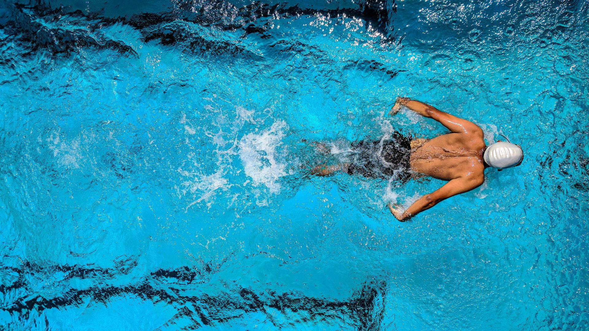 Swimming 桌布 壁紙 — 一名戴白色泳帽的泳者從俯視角度在充滿活力的藍色泳池水中滑行。