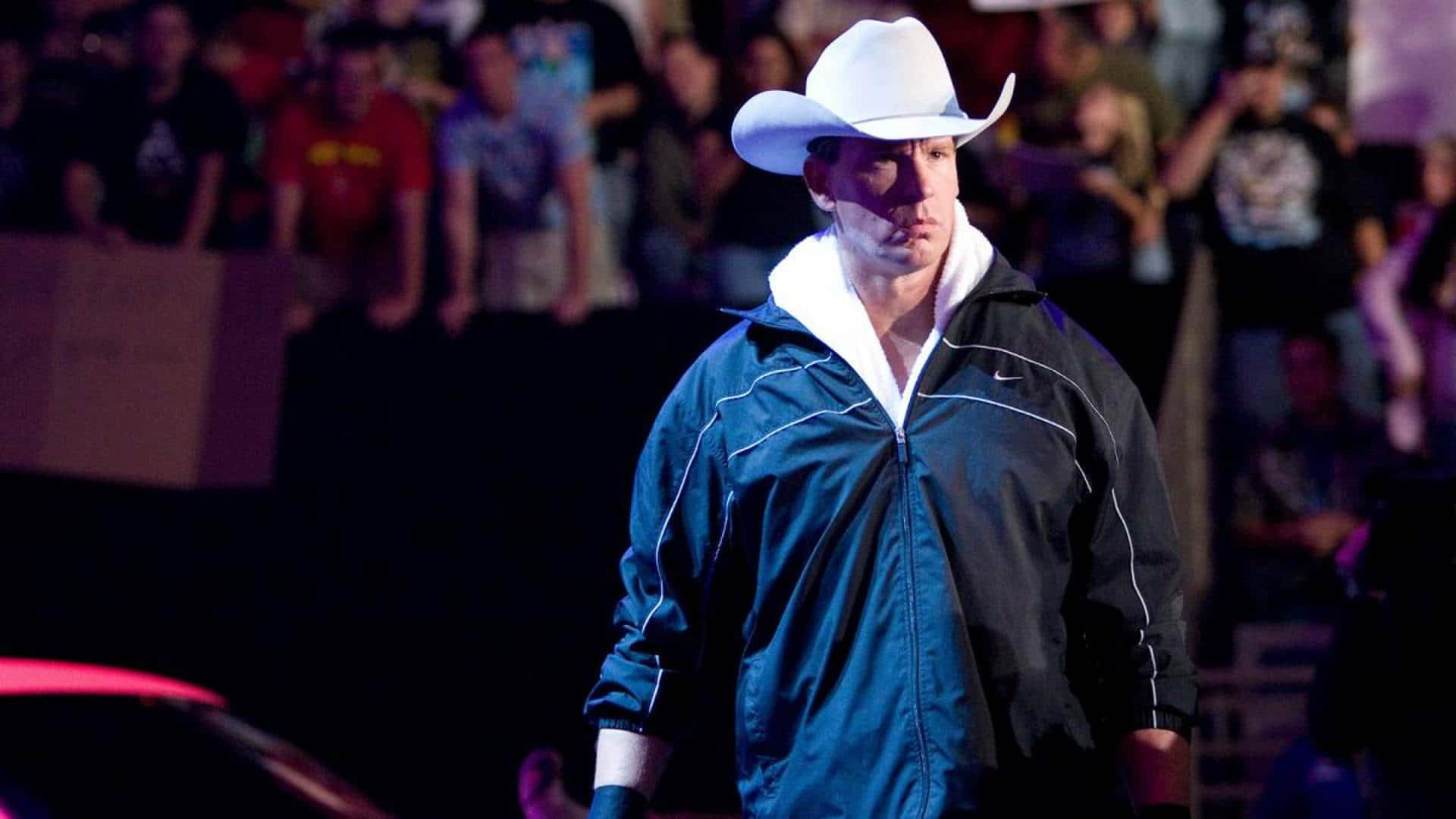 WWE 桌布 壁紙 — 一名戴白色牛仔帽、穿藍色外套的男子自信地穿過昏暗的人群，參加現場活動。