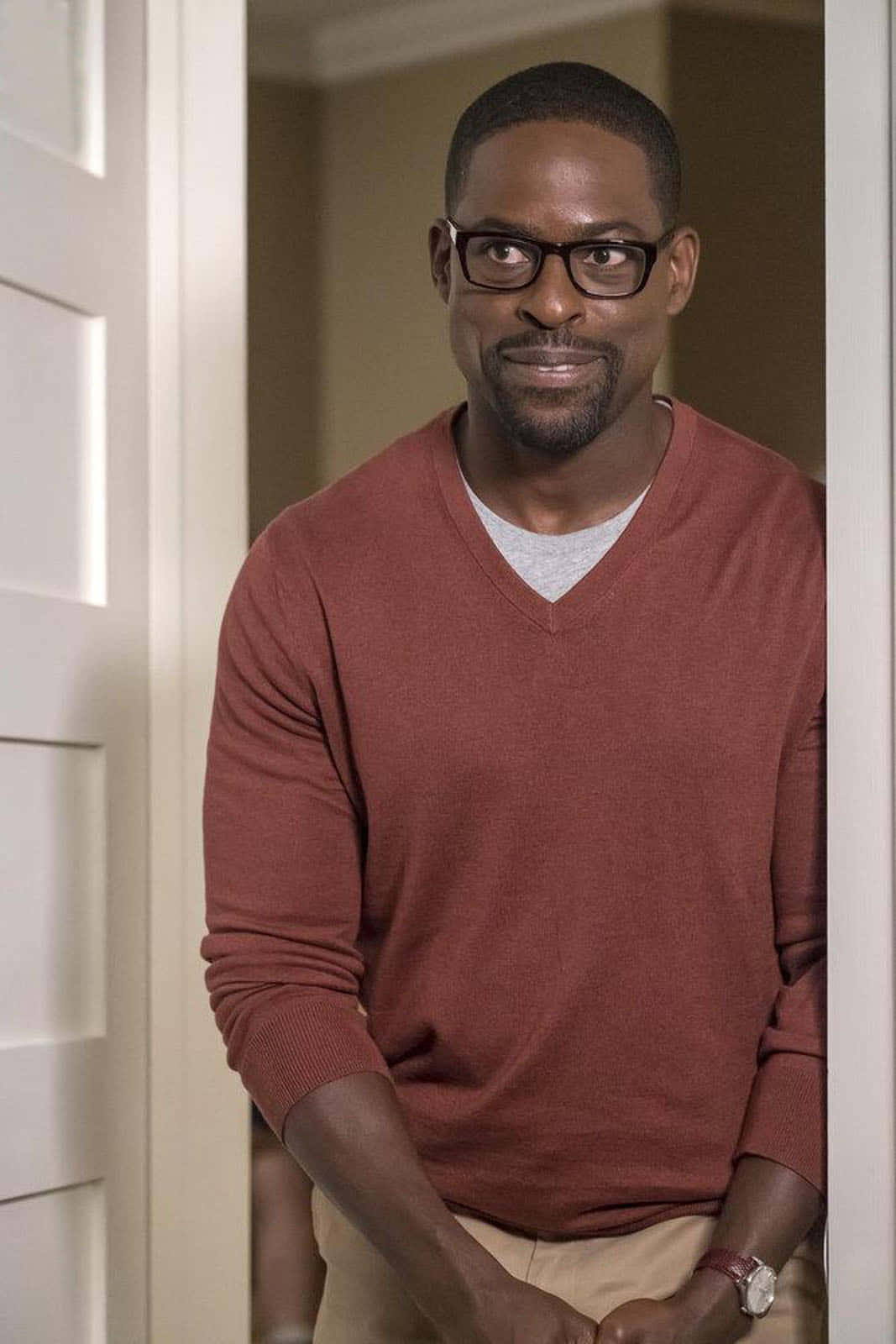 Sterling K Brown 桌布 壁紙 — 一名戴眼鏡、笑容溫暖的男子身穿鏽紅色毛衣，從白色門口探出頭來。