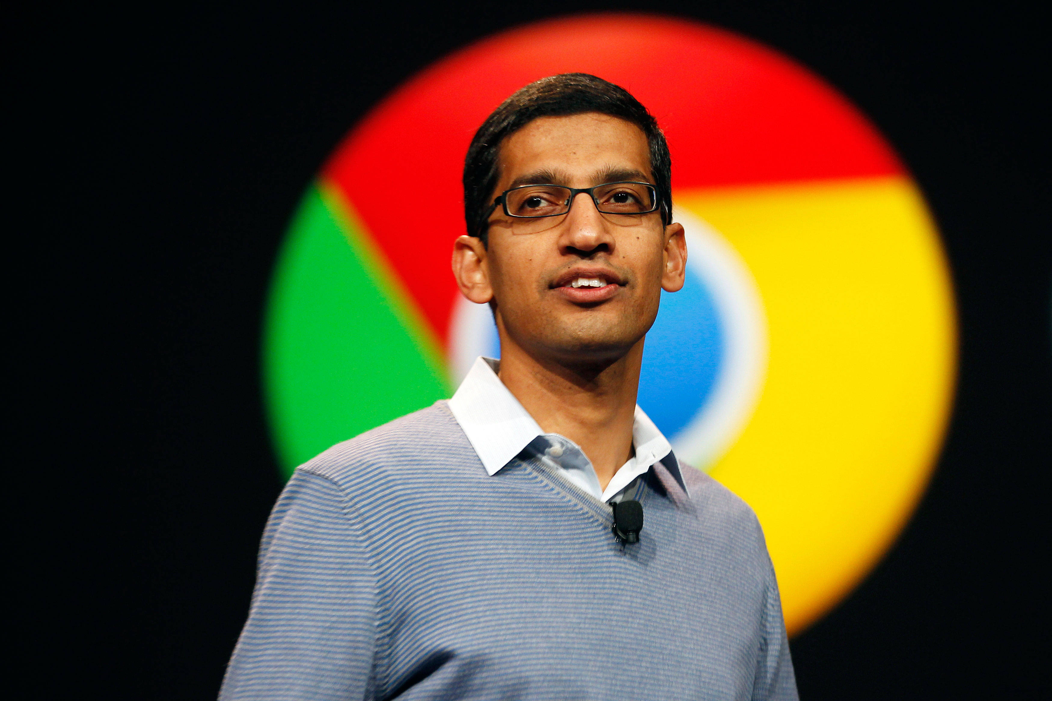 google 桌布 壁紙 — 一名戴眼鏡、身穿條紋毛衣的男子站在模糊的 Google Chrome 標誌背景前微笑。